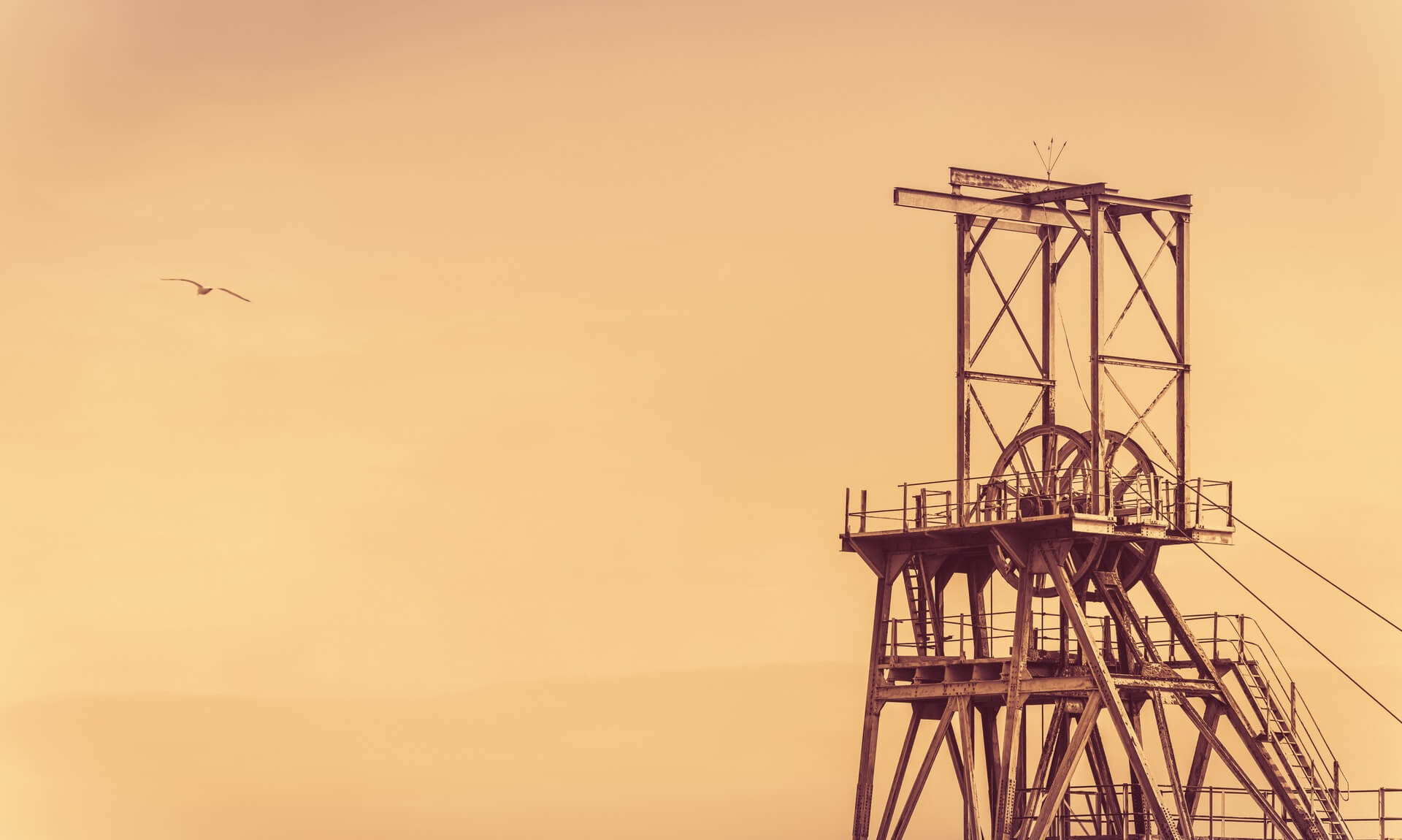 Sepia photo of a Cornish tin mine winding-gear headframe against the sky
