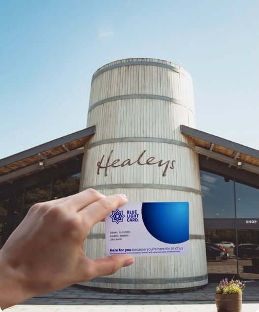 A Blue Light Card held up in front of the barrel-shaped entrance building at Healeys Cornish Cyder Farm
