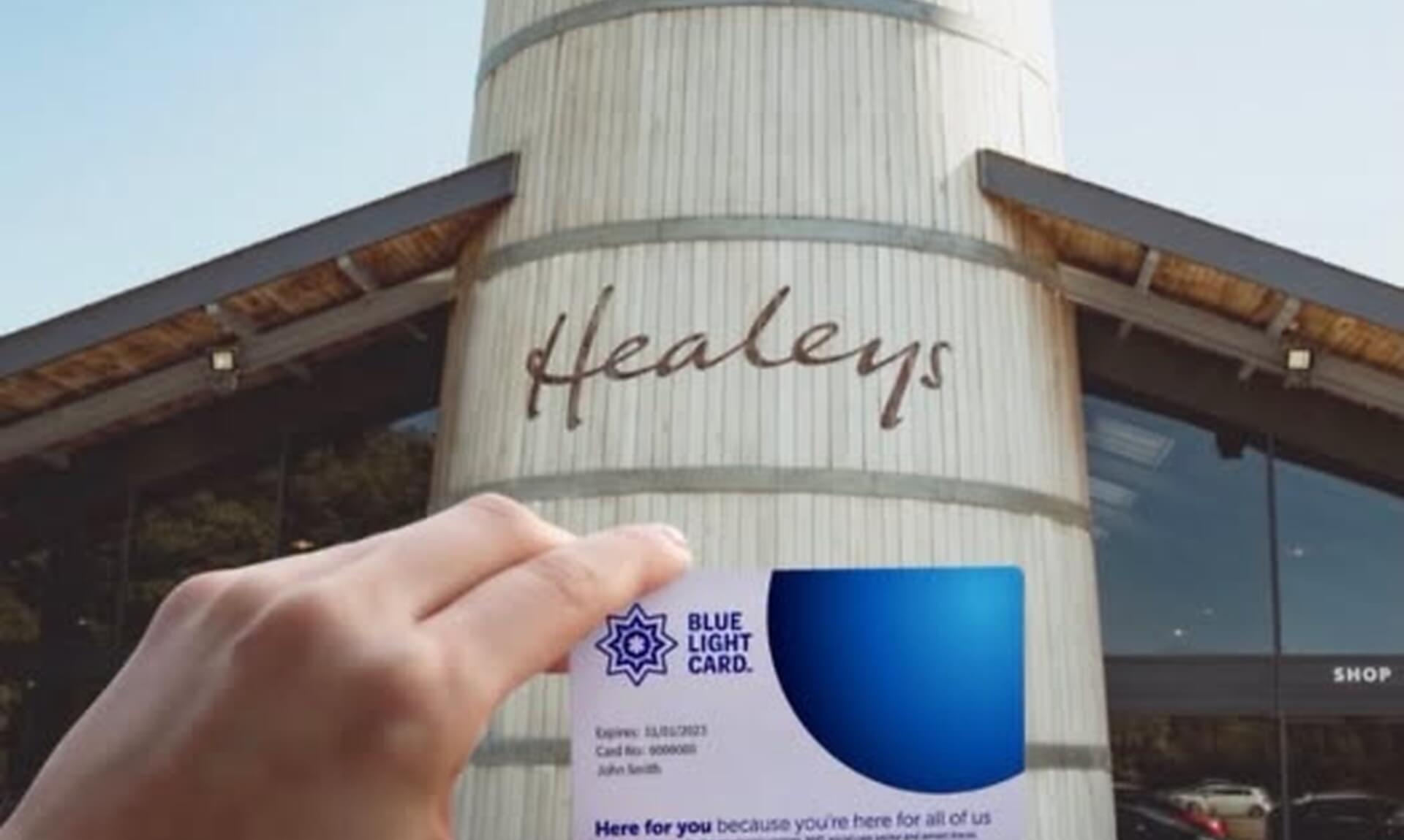 A Blue Light Card held up in front of the barrel-shaped entrance building at Healeys Cornish Cyder Farm