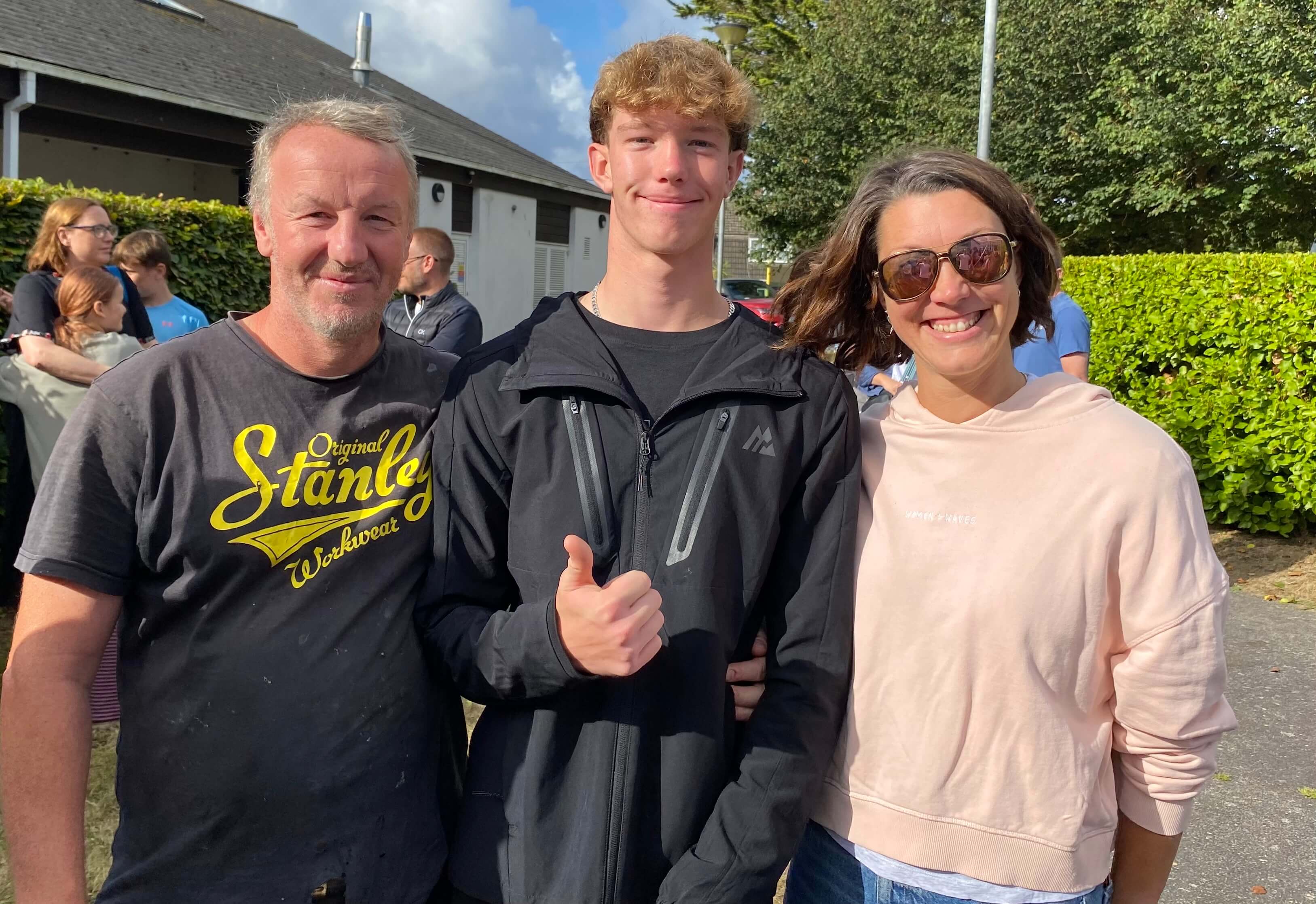 A Treviglas Academy student giving a thumbs up between two family members on GCSE results day