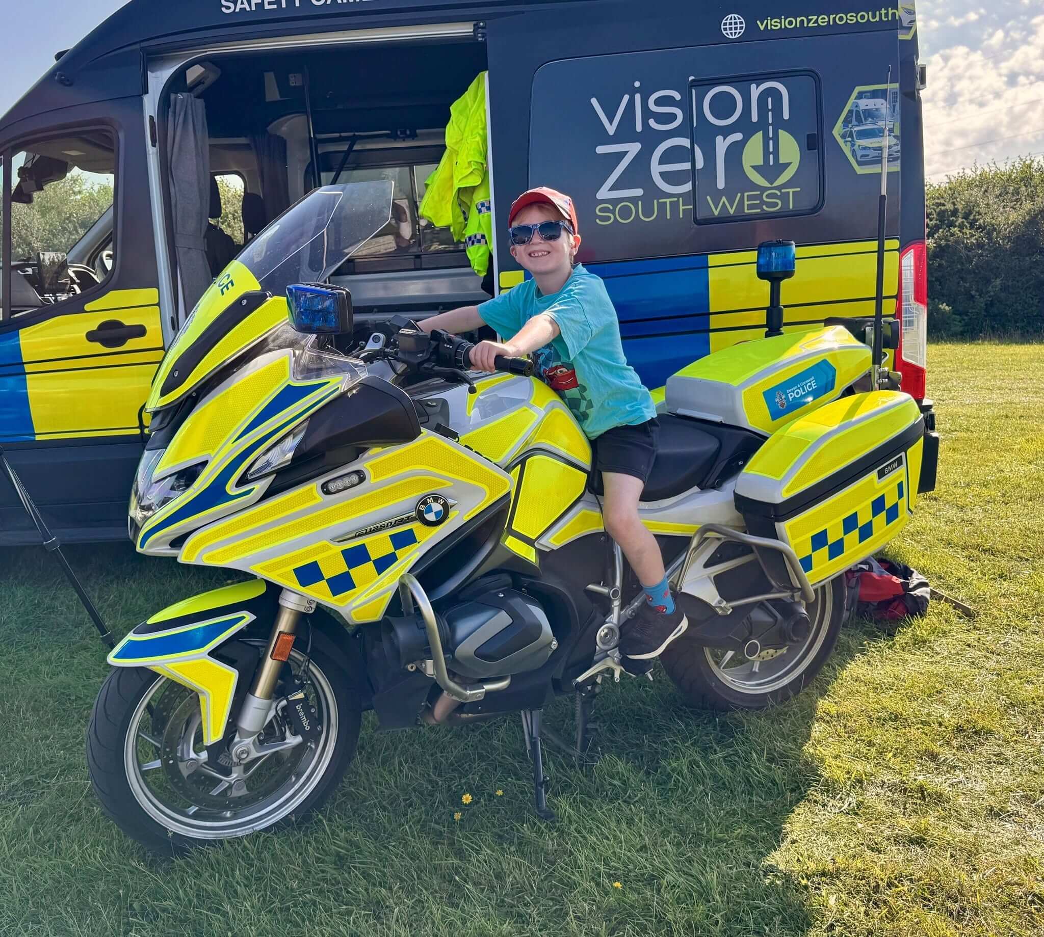 A boy in sunglasses and a red cap sits on a Devon and Cornwall Police BMW motorcycle at the Camelford Show
