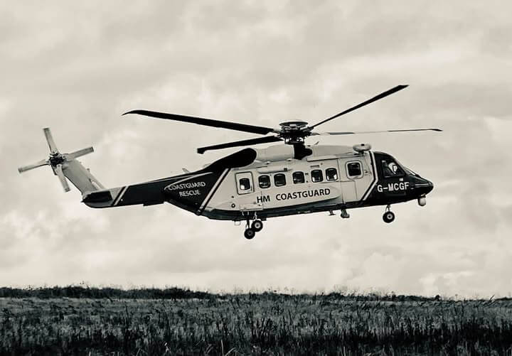 HM Coastguard search and rescue helicopter G-MCGF flying low over open ground