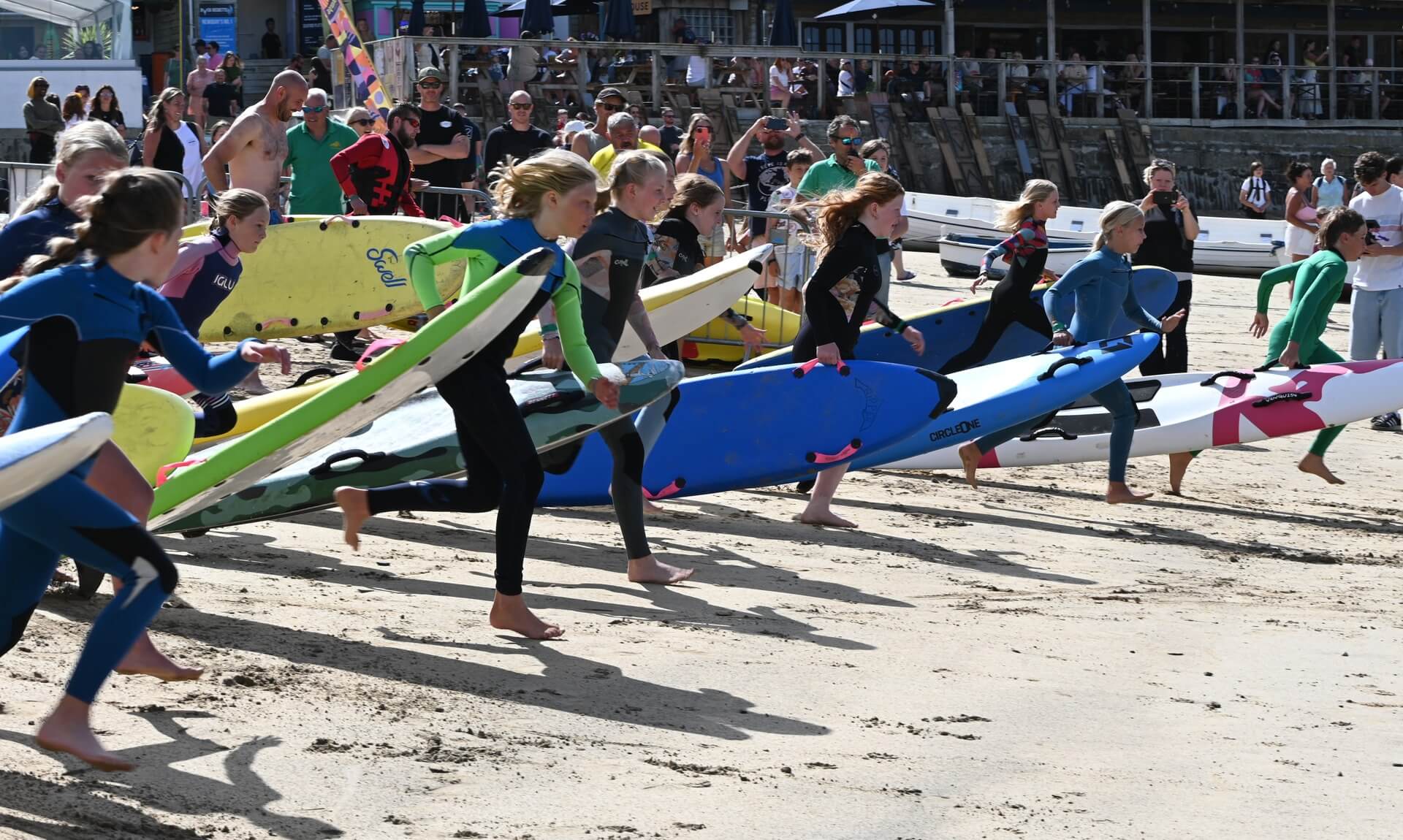 Young surf lifesavers sprint across Newquay beach carrying rescue boards as a crowd watches