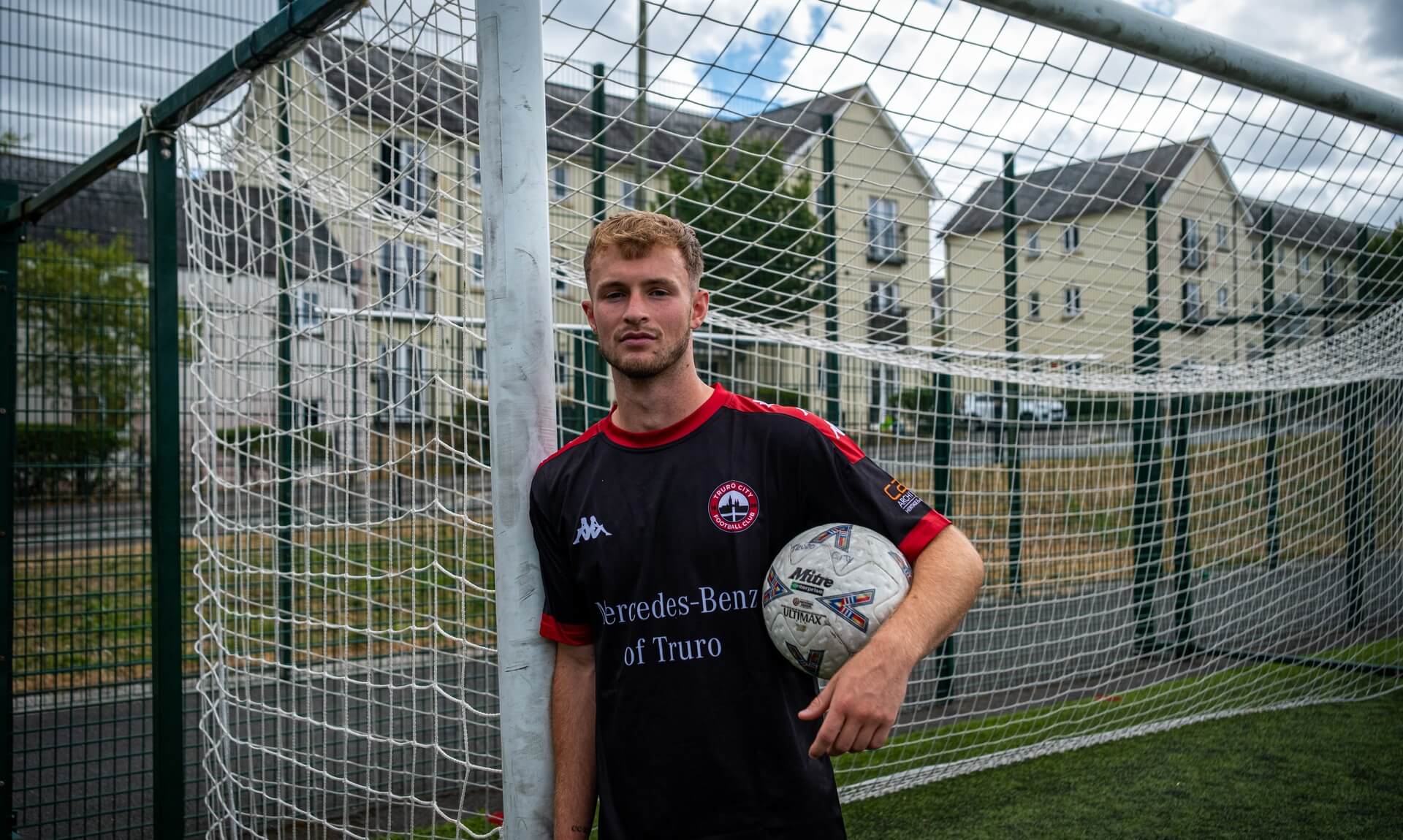 Max Kinsey leaning against a goalpost in Truro City training kit holding a football