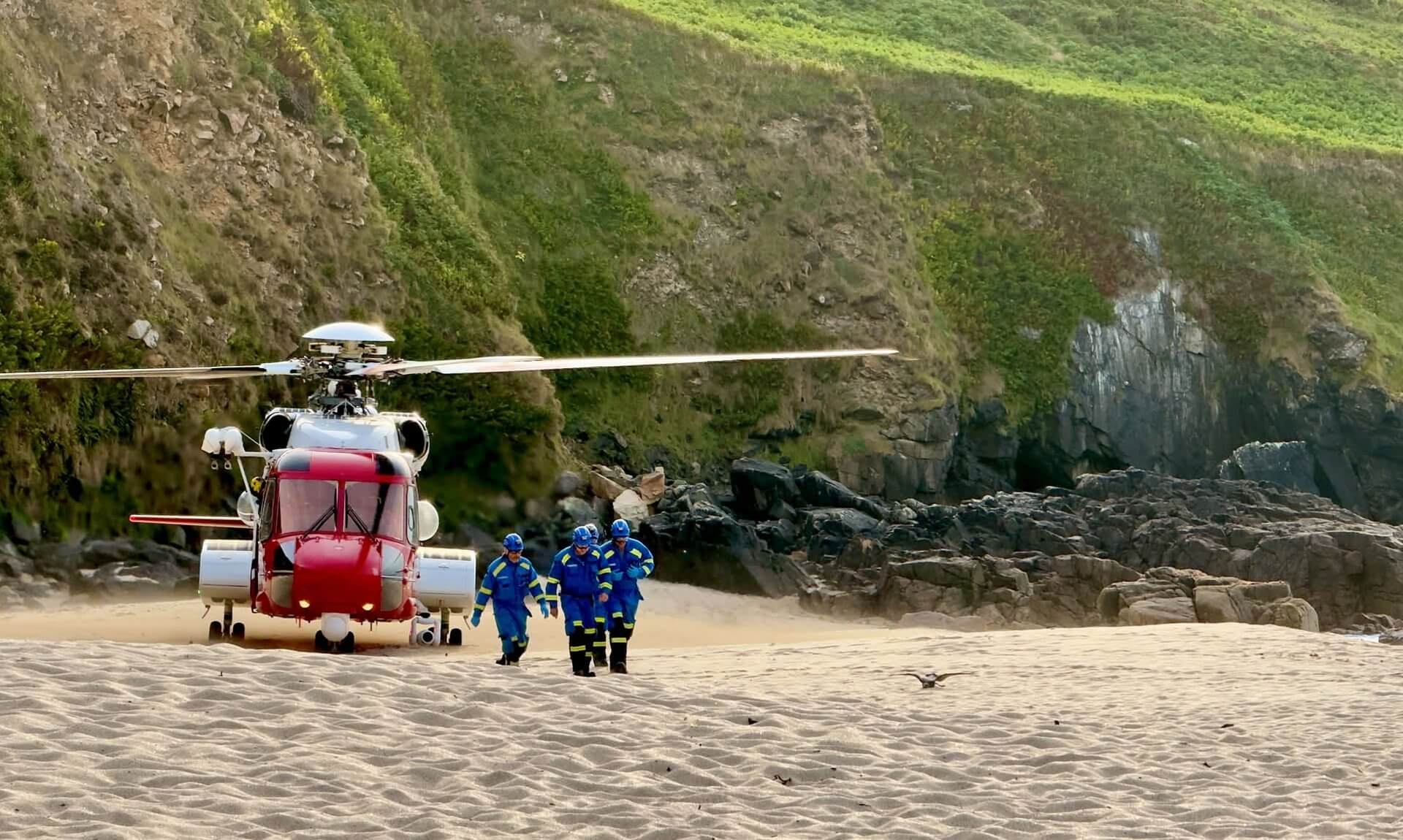 HM Coastguard helicopter landed on a Cornish beach with crew walking towards camera