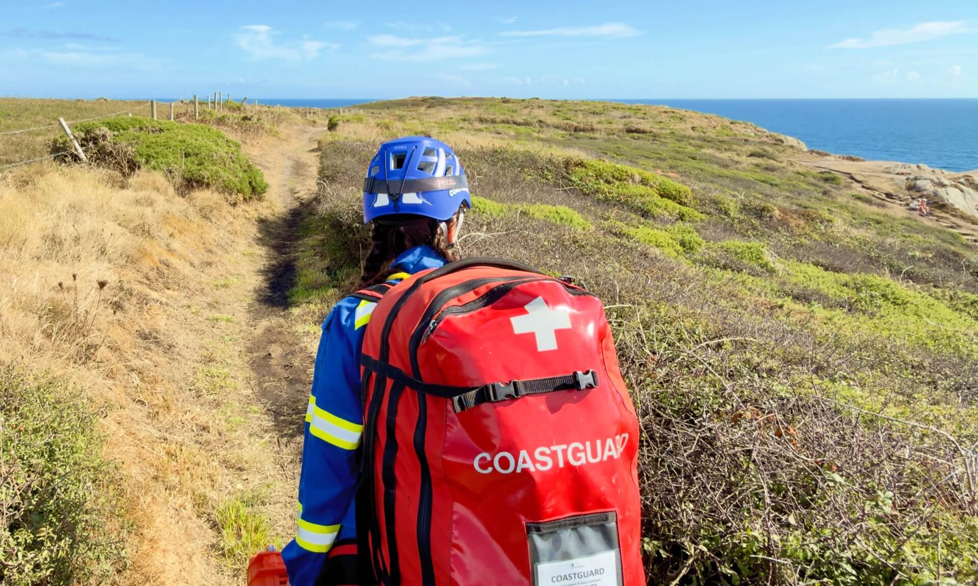 Coastguard volunteer carrying rescue kit along the coast path near Land's End