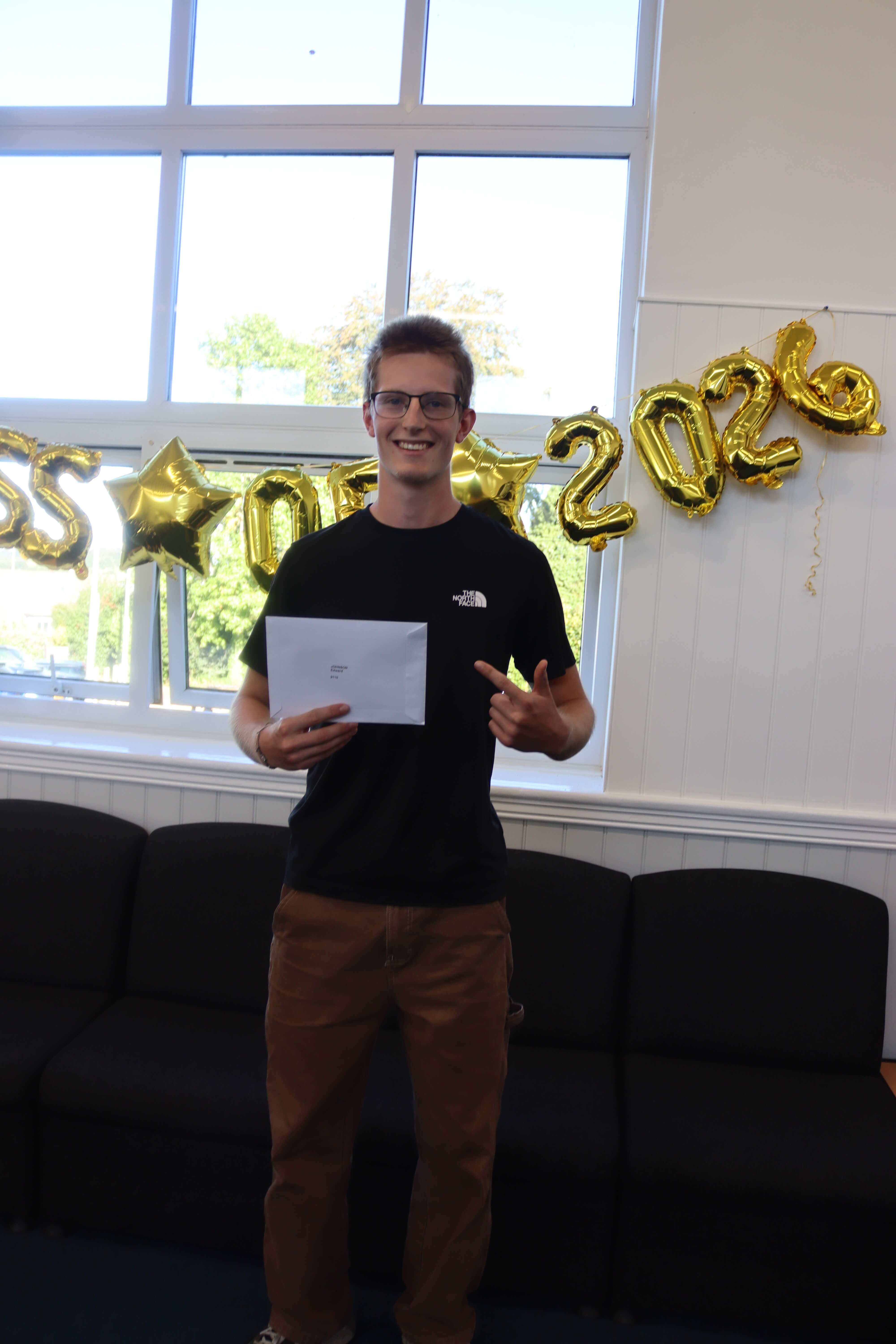 A Launceston College student smiling and pointing at his A Level results envelope on results day 2026