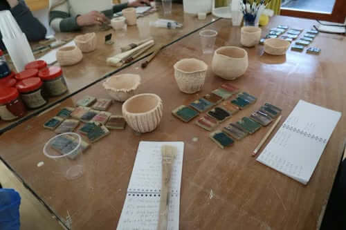 A workshop table covered with unfired pots, glaze jars, test tiles and handwritten notes