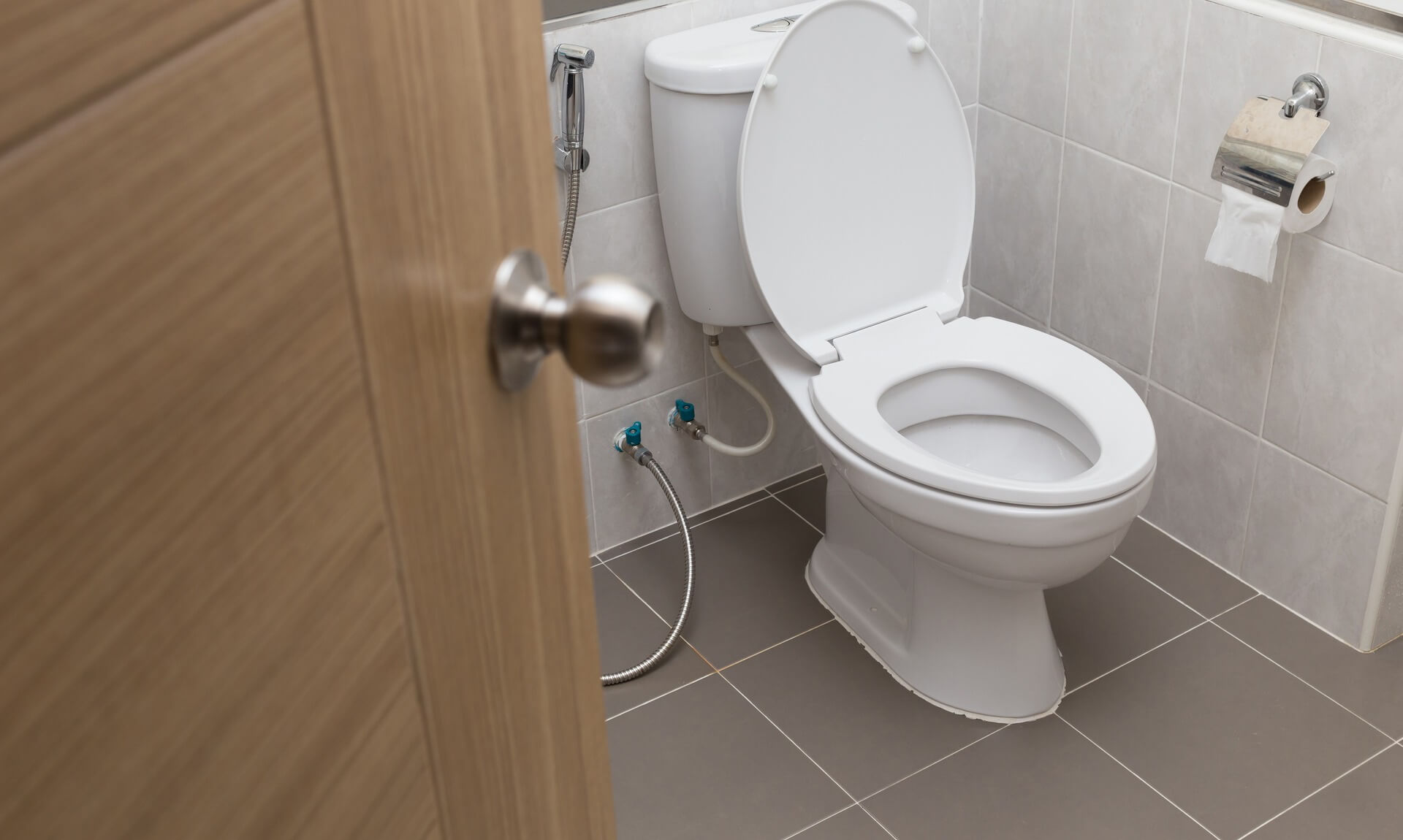 A white toilet with the lid up in a tiled bathroom, cistern and supply pipes visible