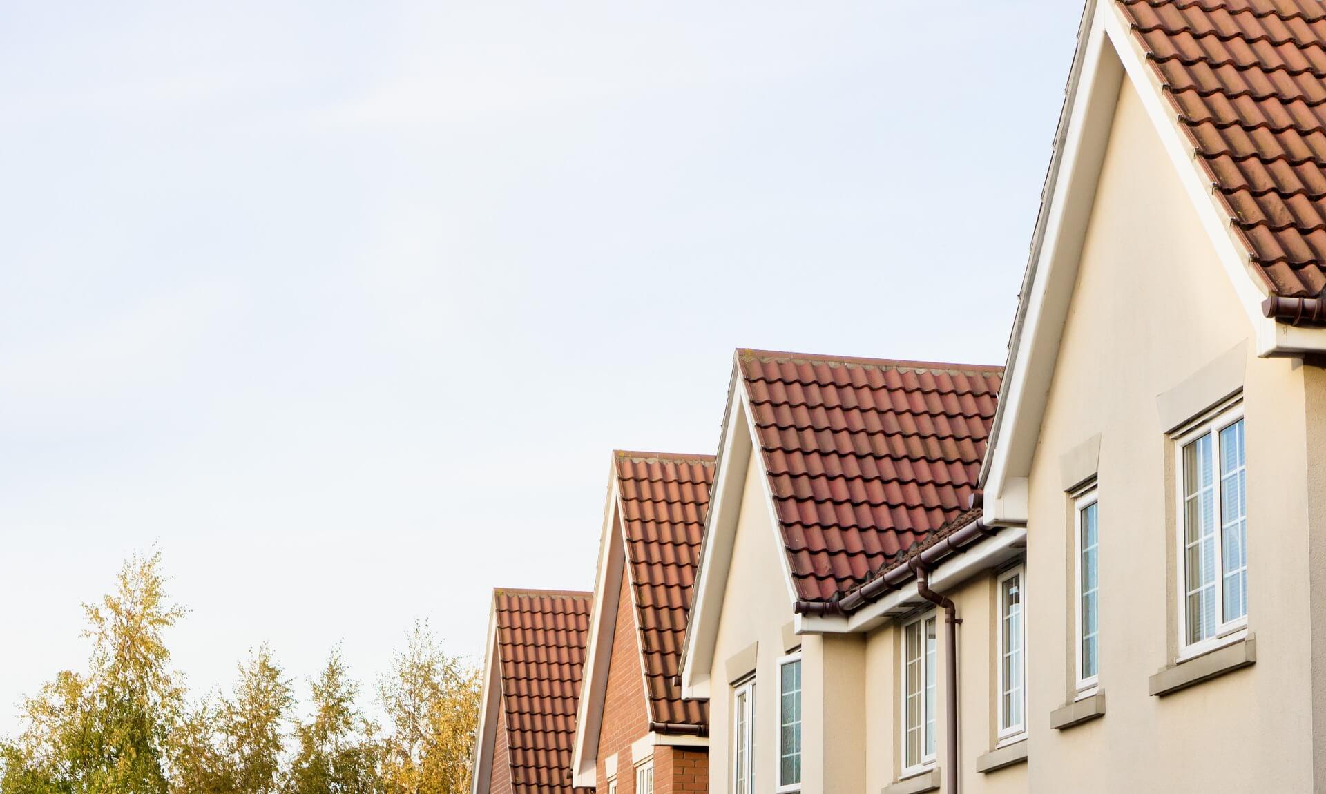 A row of new-build houses with red-tiled roofs against a clear sky