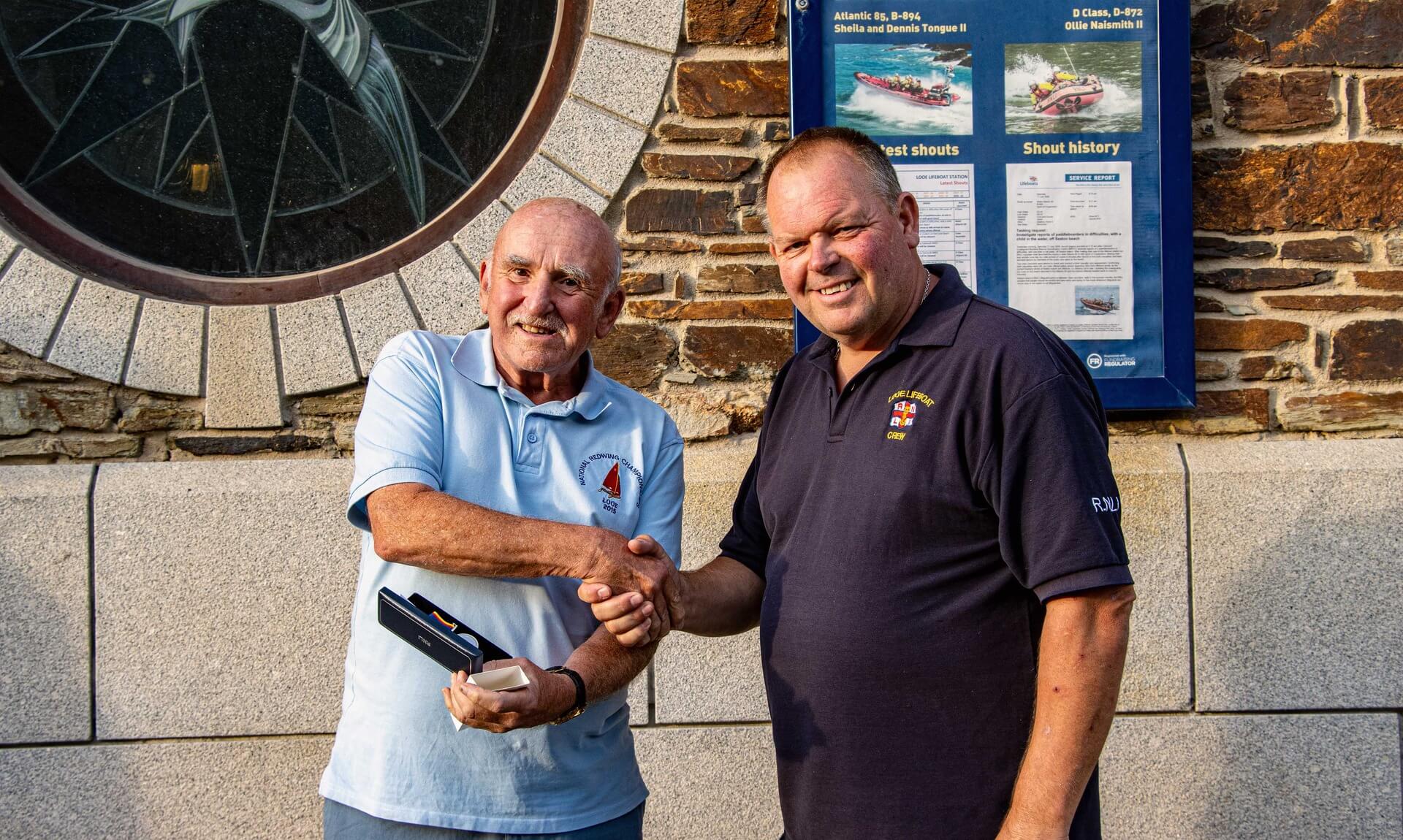 Looe RNLI Lifeboat Operations Manager Clive Palfrey shakes hands with volunteer Paul Sedgbeer as he presents his 20 year long service award outside the Albatross Boathouse.