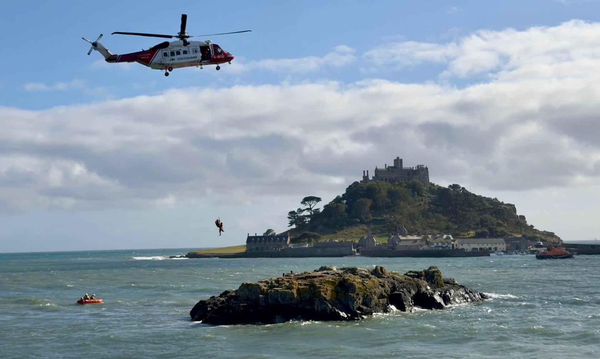 HM Coastguard helicopter Rescue 924 winches a person from the sea near St Michael's Mount at Marazion