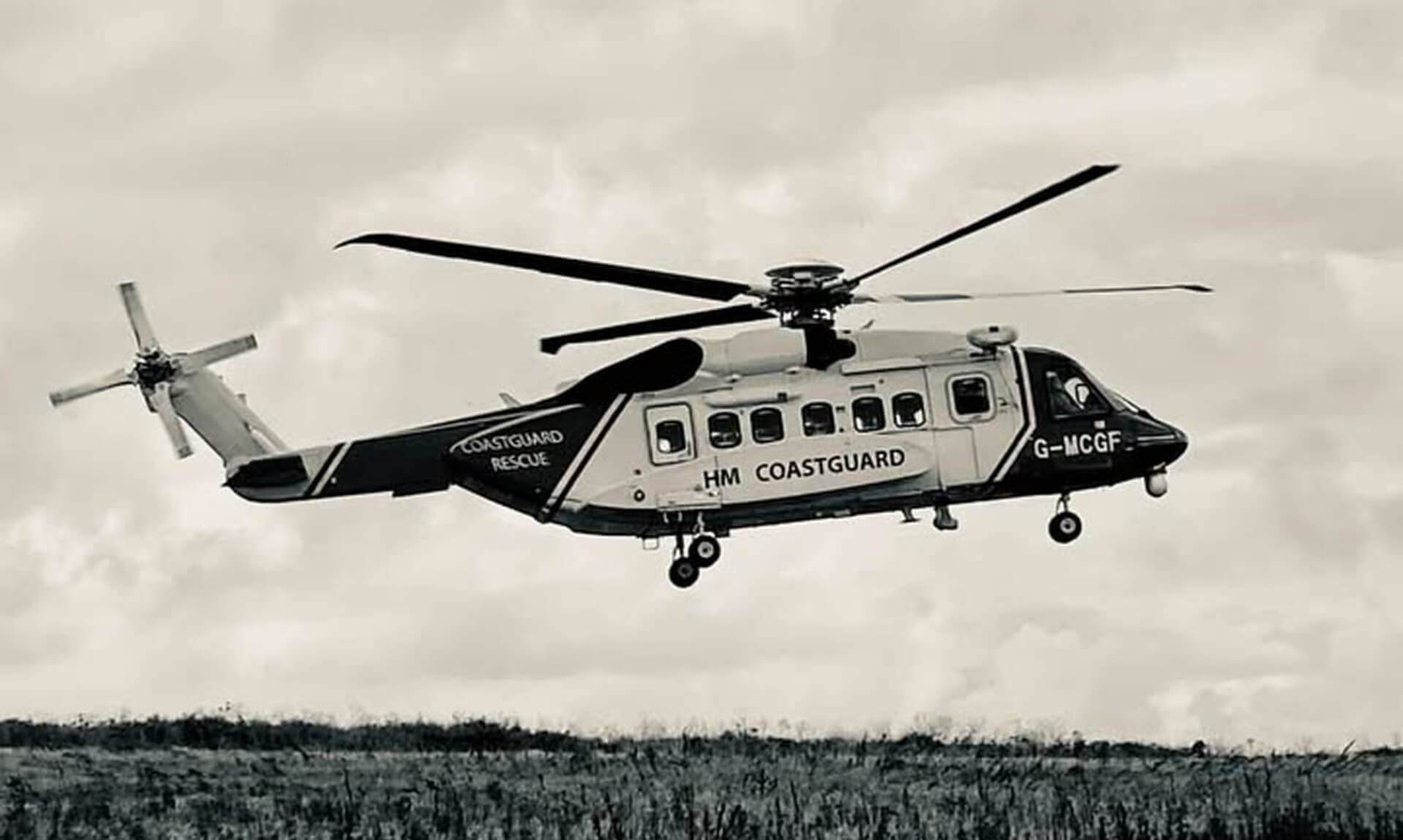 HM Coastguard search and rescue helicopter G-MCGF flying low over open ground