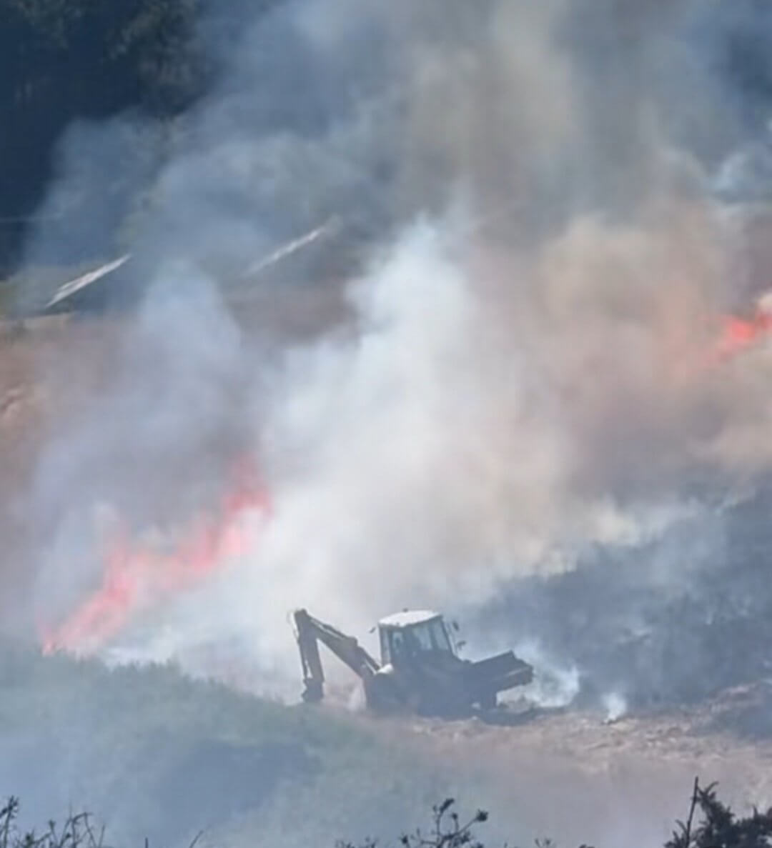 Digger working in thick smoke cutting a fire break at Mawgan Porth wildfire