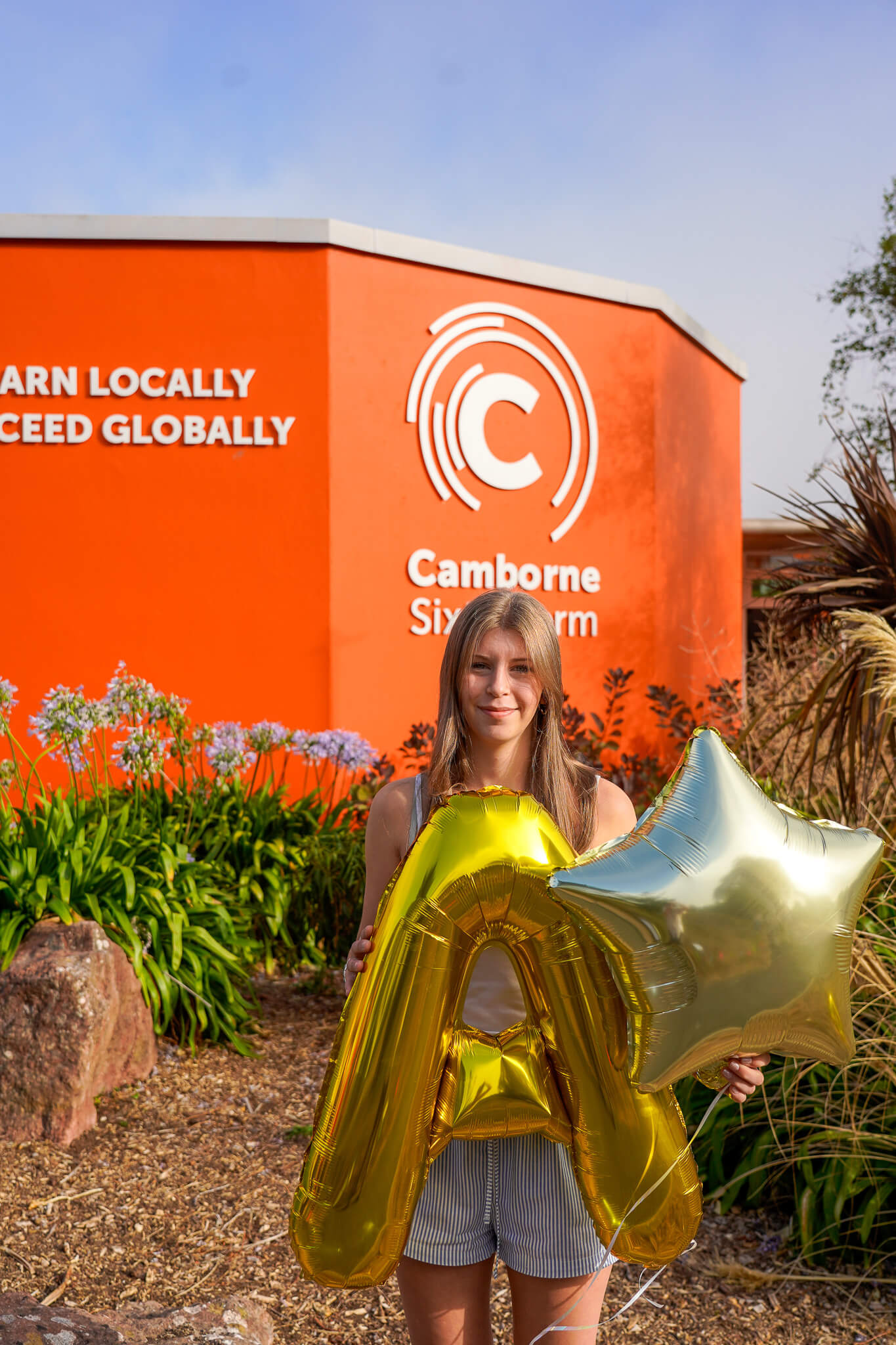 Camborne Sixth Form student Milly P holding gold A and star balloons outside the college on A-level results day