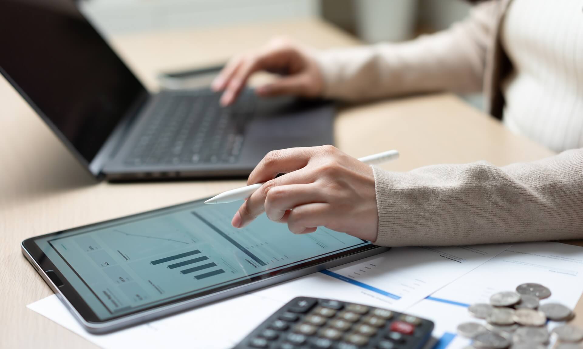 Person reviewing financial figures on a tablet beside a laptop and calculator