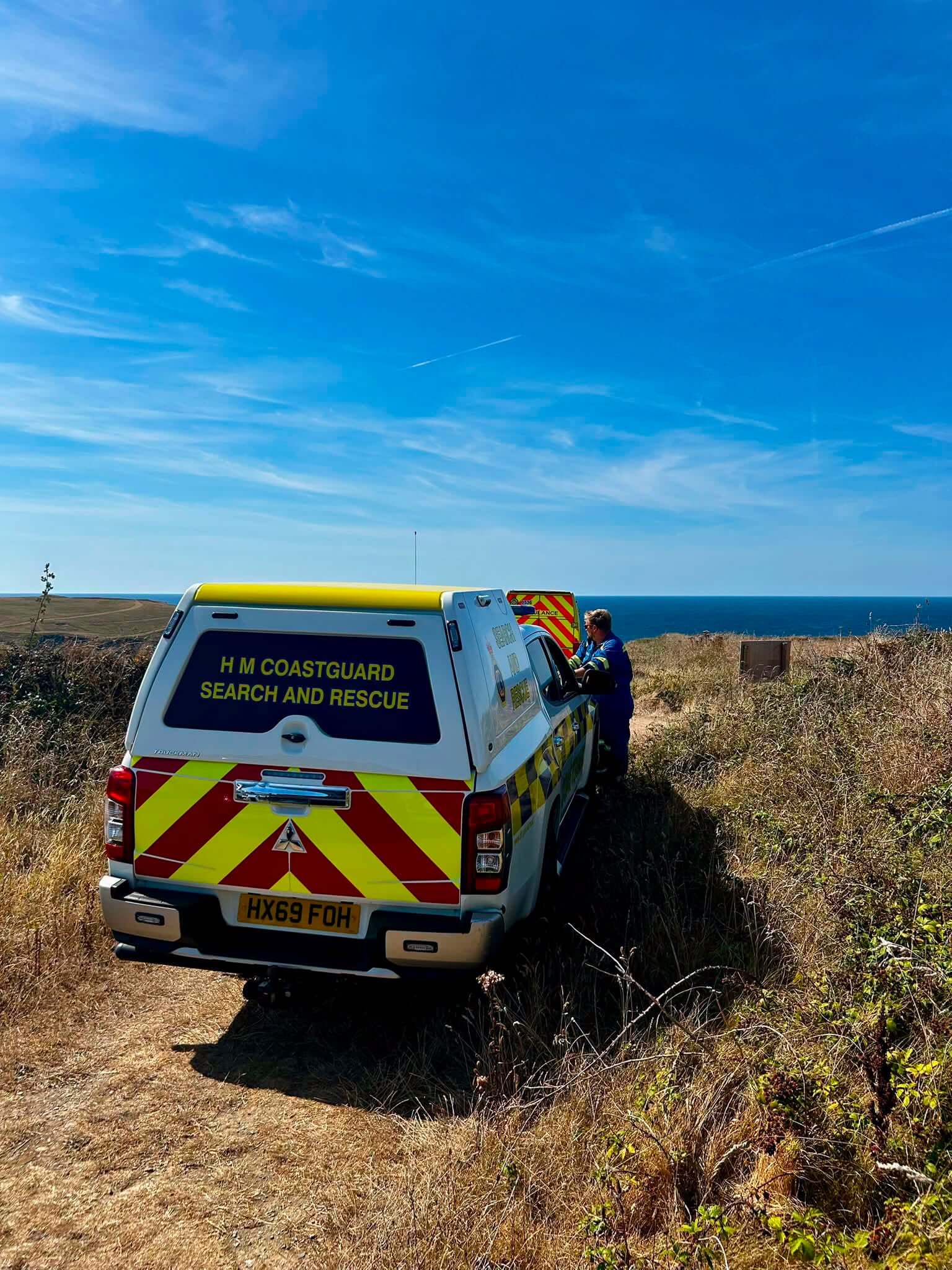 HM Coastguard search and rescue vehicle parked on a clifftop above the sea near West Pentire, with a crew member alongside