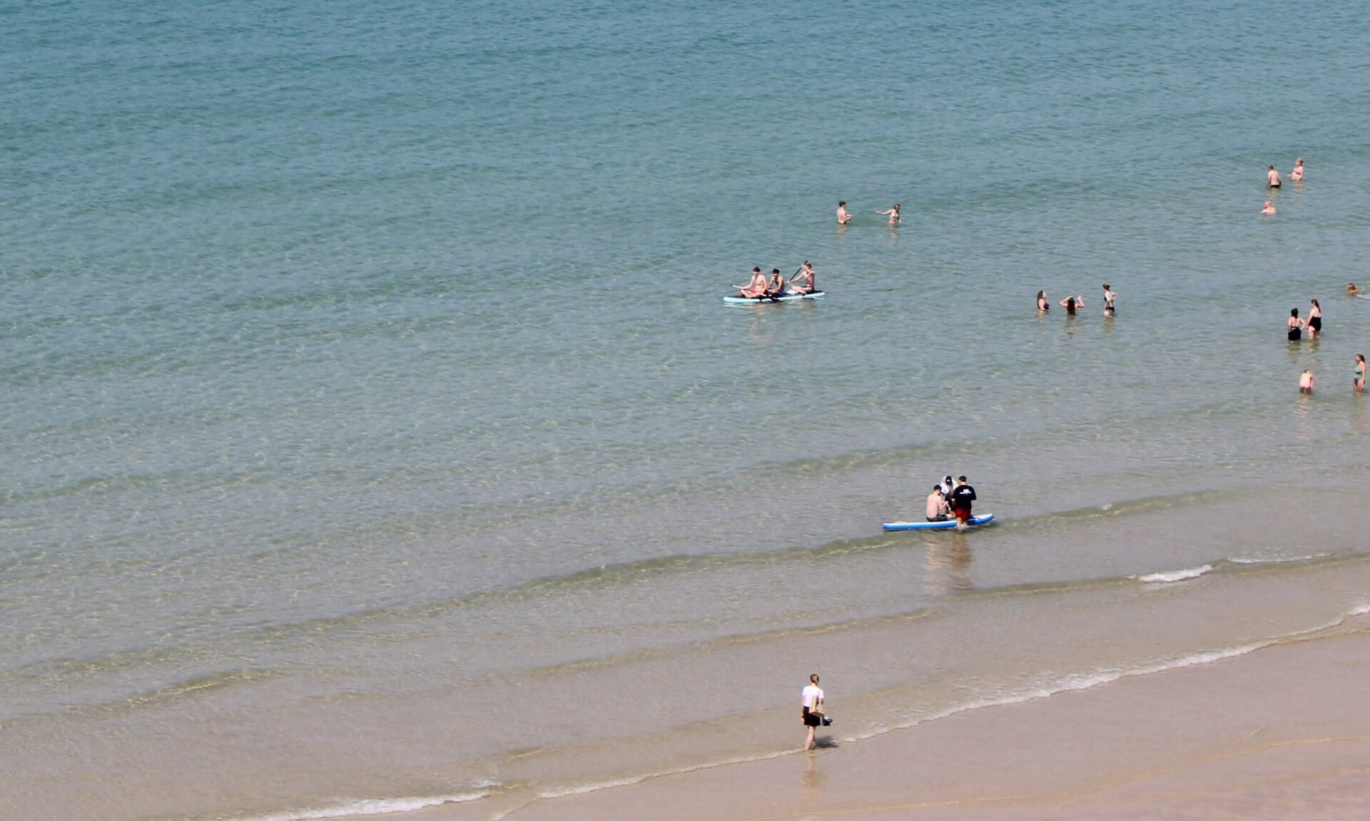 Swimmers and paddleboarders in the sea off a Newquay beach on a hot summer day
