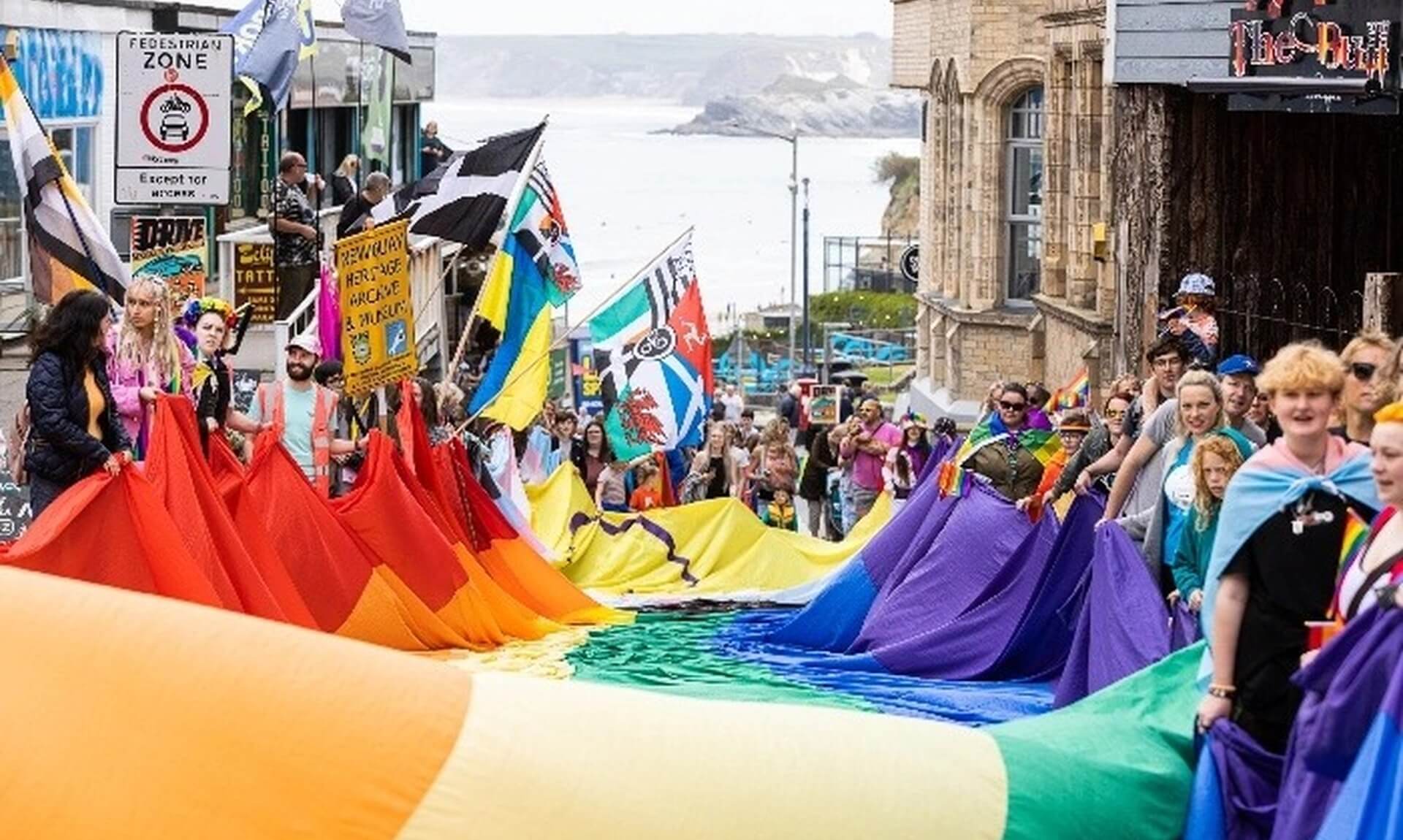 Crowds carry a huge rainbow flag down a Newquay street towards the sea during the Cornwall Pride parade