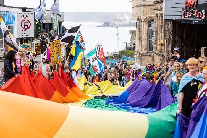Crowds carry a huge rainbow flag down a Newquay street towards the sea during the Cornwall Pride parade