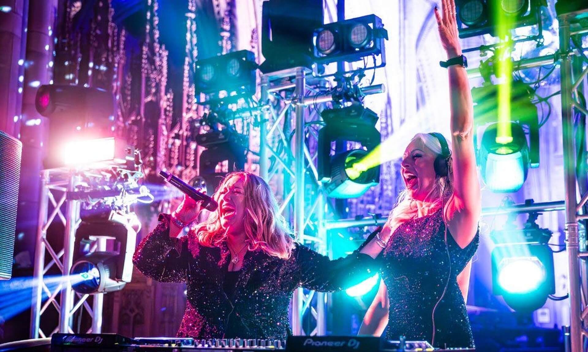 Dvotion perform on stage under coloured lighting behind Pioneer DJ decks