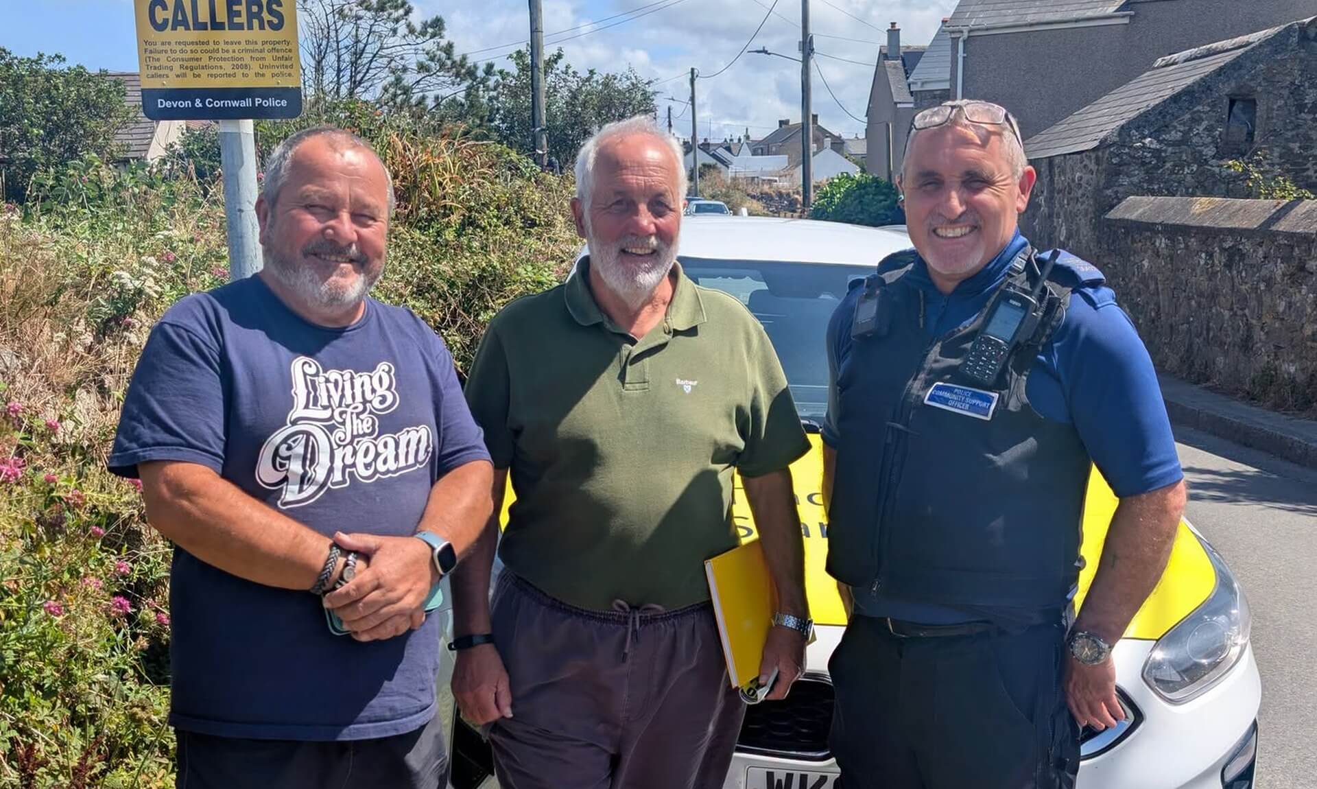 Two local residents stand with a police community support officer beside a No Cold Callers sign on a Cornish street