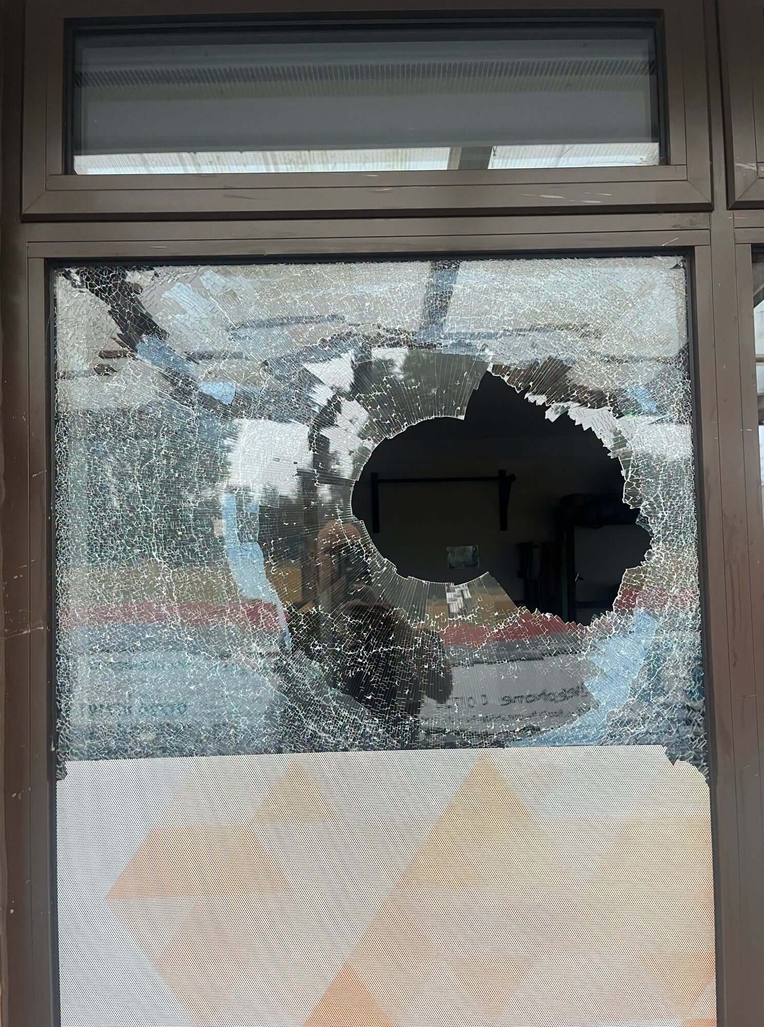 Close-up of a smashed window at Par Track with a brick-sized hole through the glass
