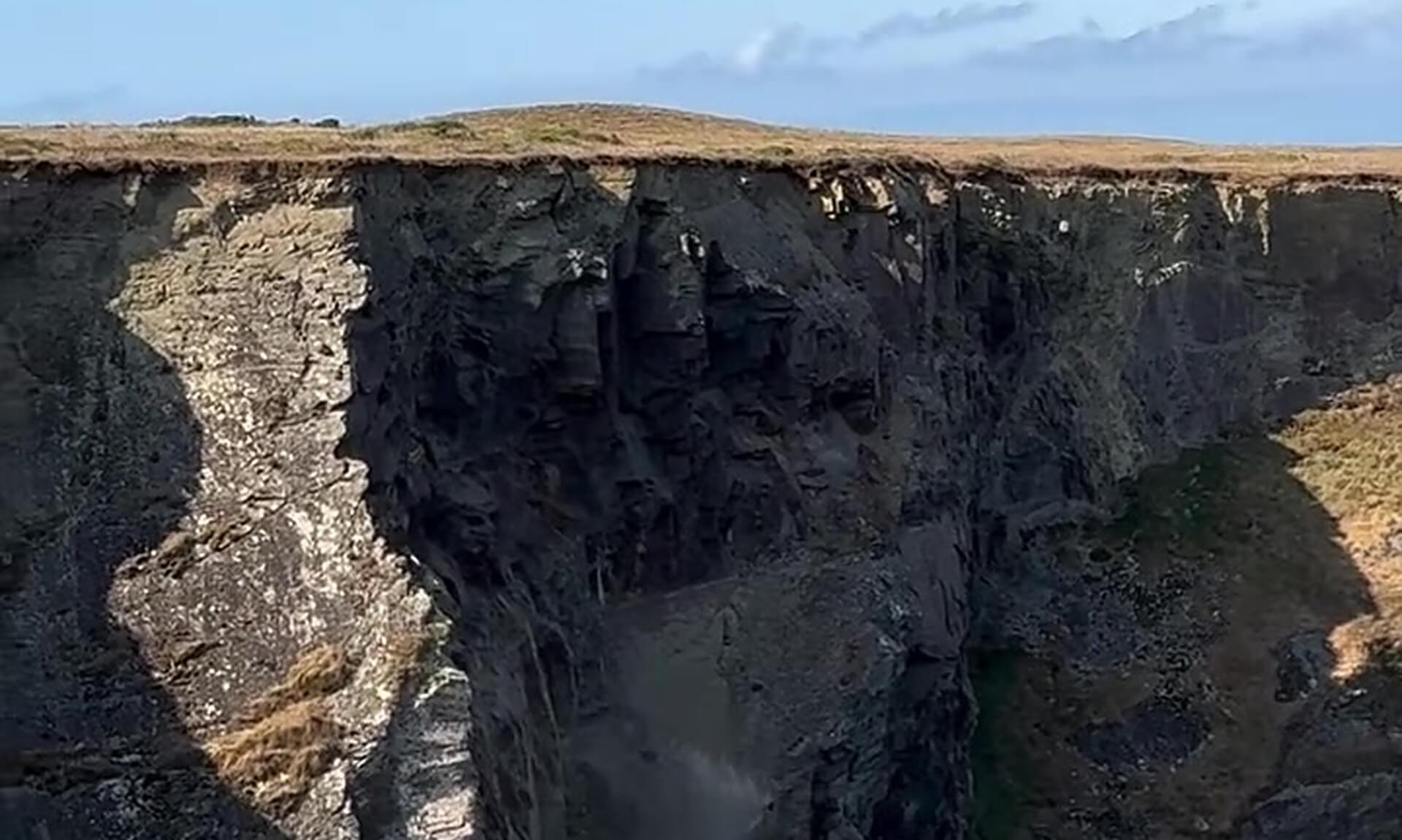 Rock and dust falling down a dark cliff face at Park Head near Bedruthan Steps