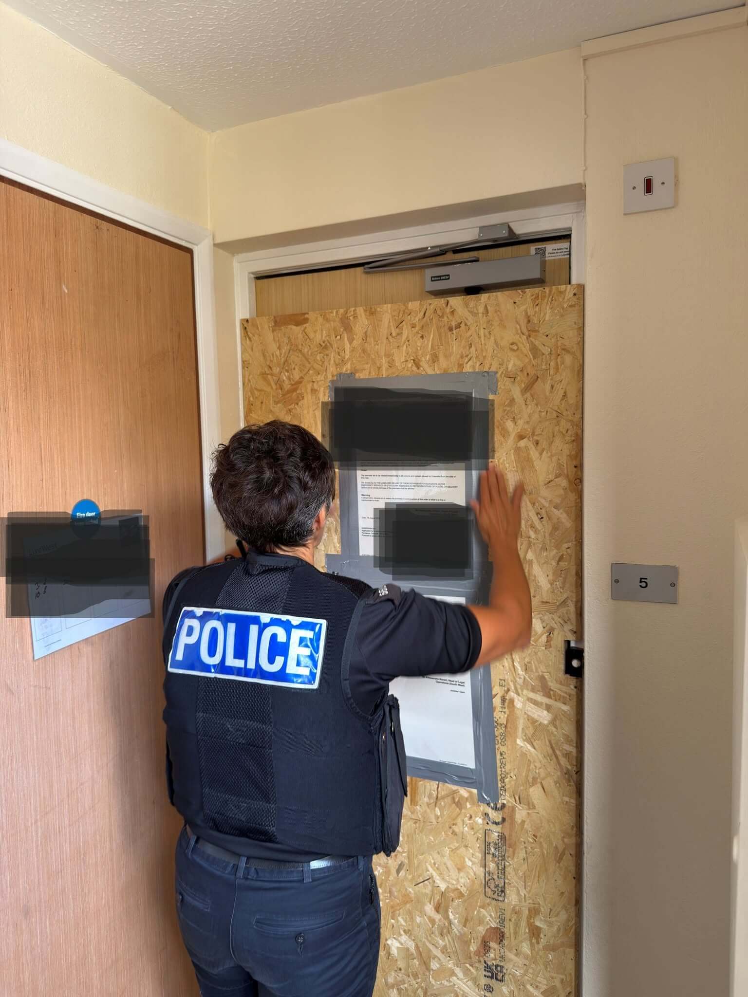 Police officer fixing a closure order notice to a boarded-up door in Penzance