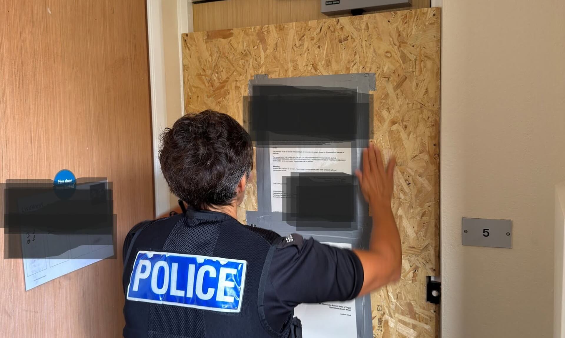 Police officer fixing a closure order notice to a boarded-up door in Penzance