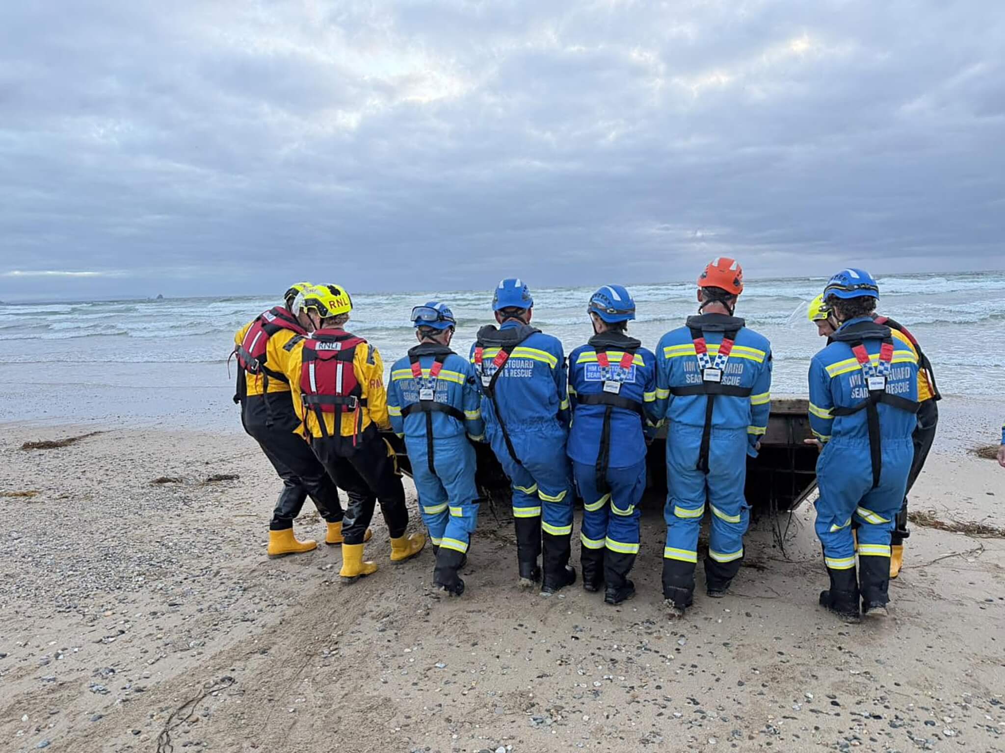 Coastguard and RNLI crews stand at the water's edge beside the recovered platform at Perranporth