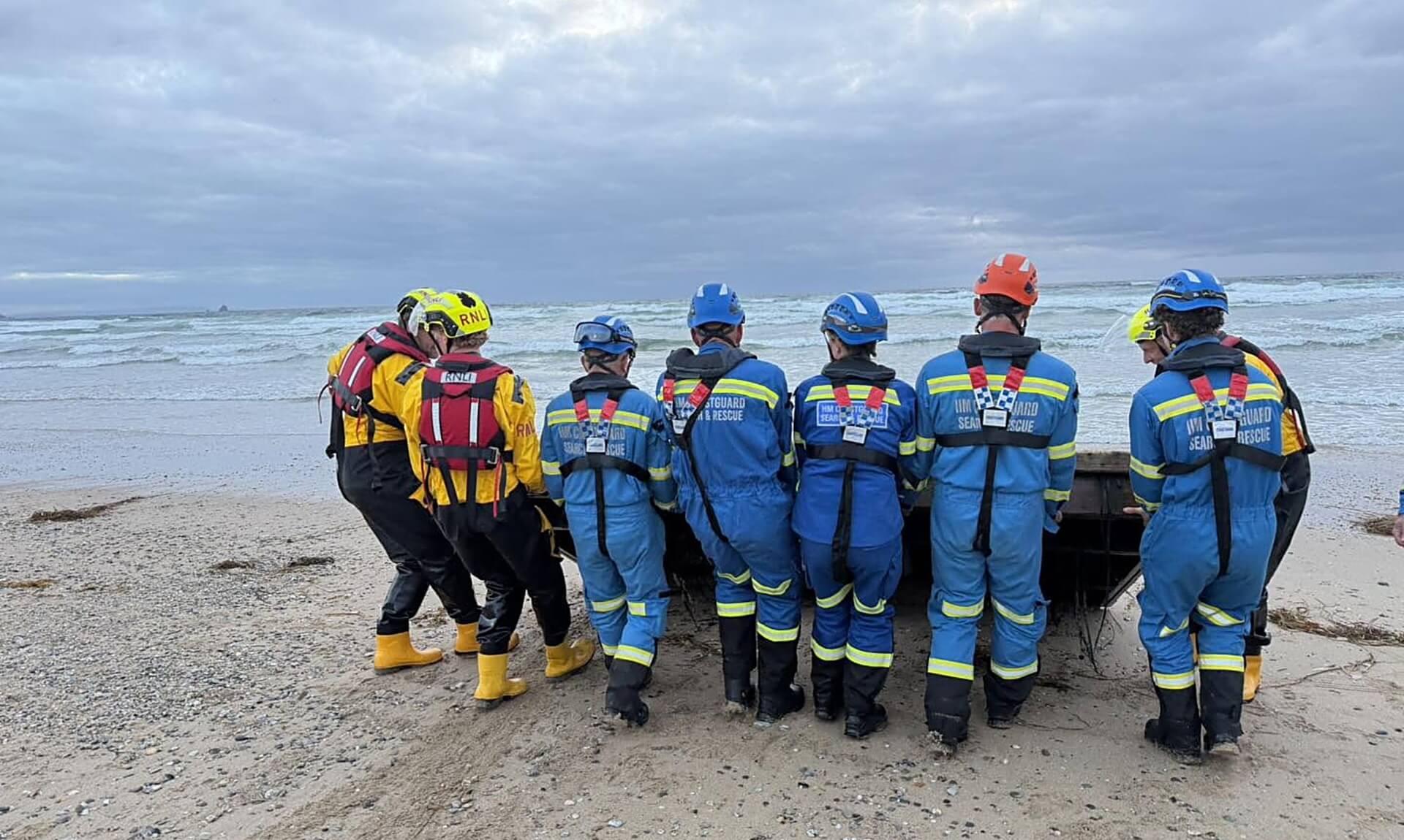 Coastguard and RNLI crews stand at the water's edge beside the recovered platform at Perranporth