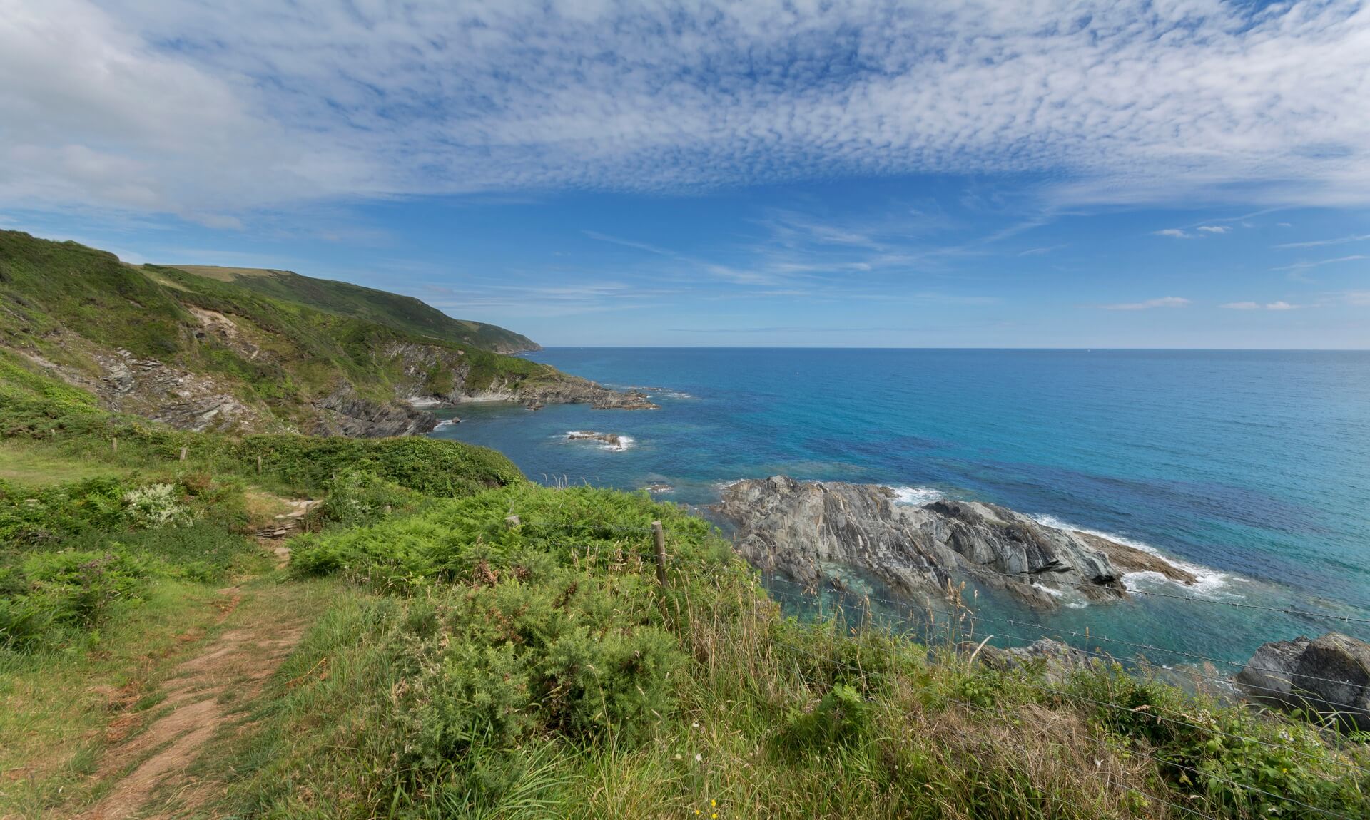 The cliffs and rocky shoreline of Lantivet Bay on the south coast of Cornwall under a blue sky