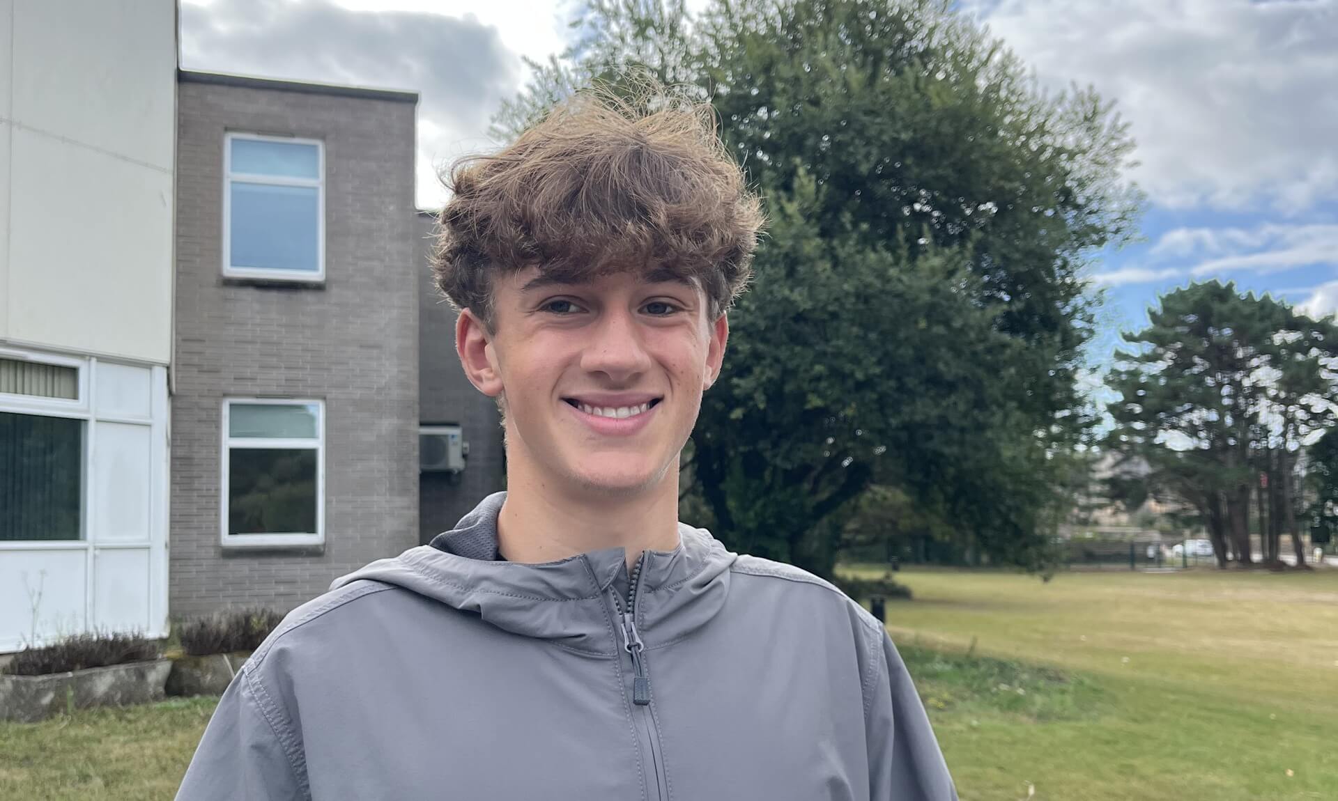 A smiling Pool Academy student holding his GCSE results envelope