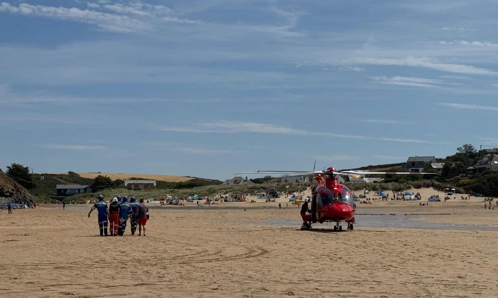 Cornwall Air Ambulance helicopter on Porthcothan beach with rescue team walking across the sand