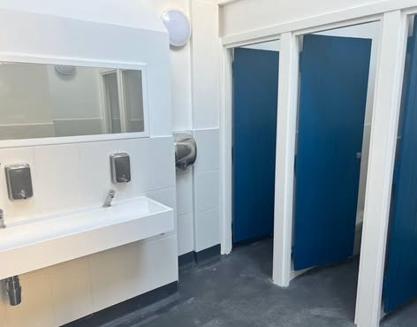 Interior of the Porthgwidden public toilets in St Ives, with a white sink unit and blue cubicle doors