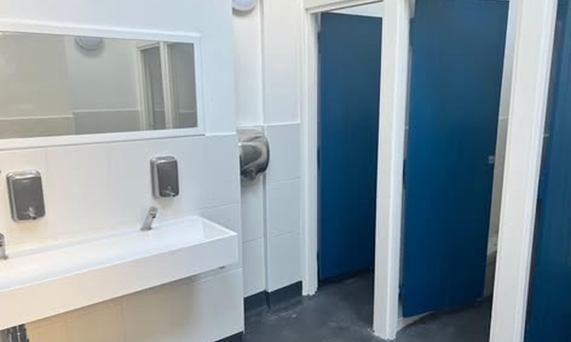Interior of the Porthgwidden public toilets in St Ives, with a white sink unit and blue cubicle doors