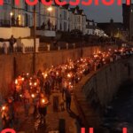 Crowds carrying lit torches along Porthleven harbour wall at night