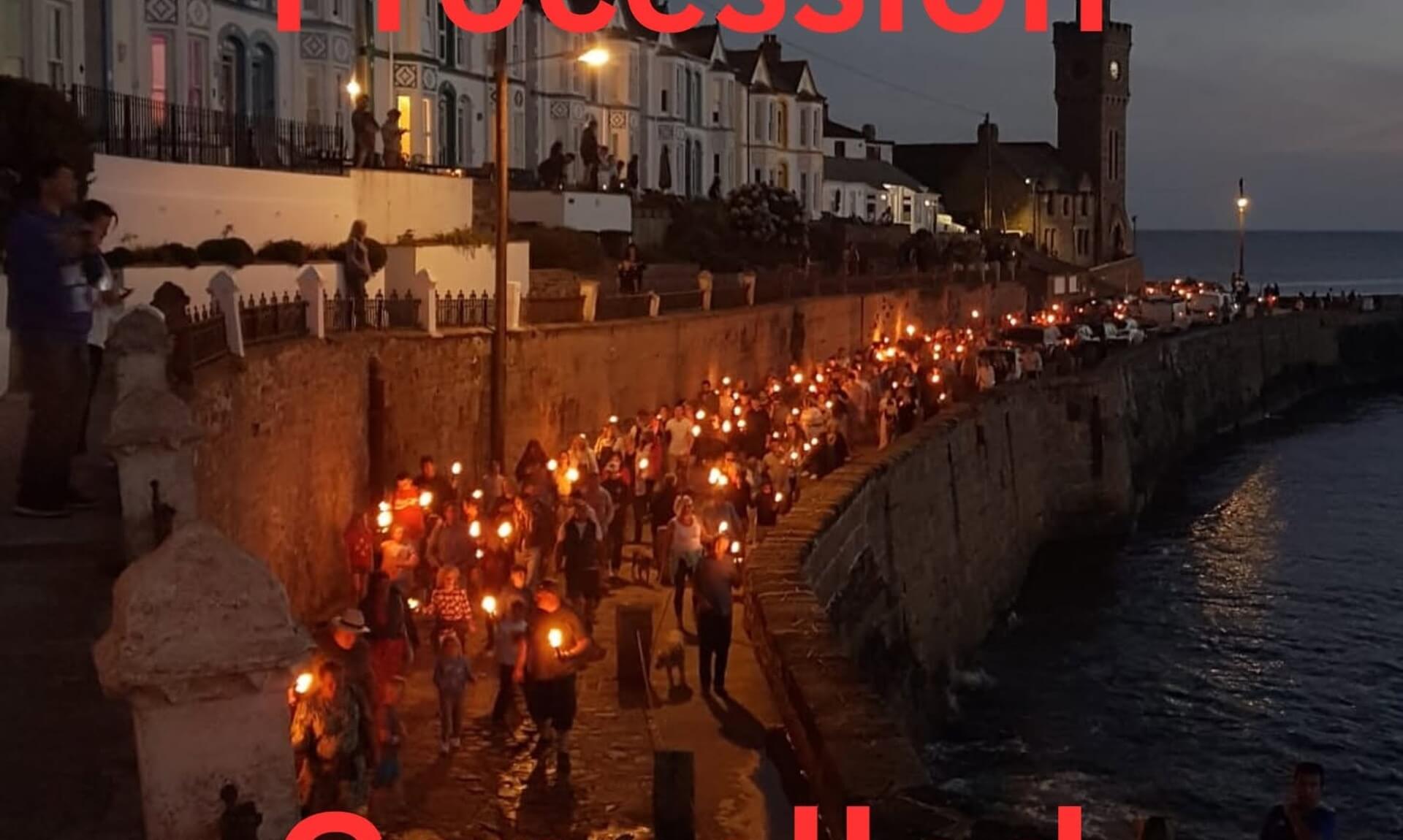 Crowds carrying lit torches along Porthleven harbour wall at night