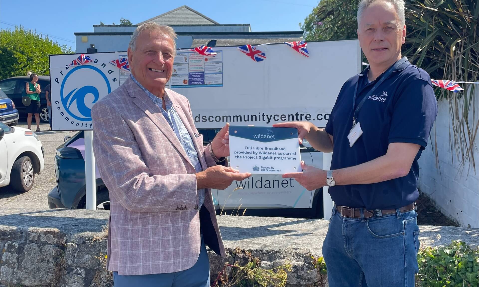 Peter Thompson and Simon Hughes holding a Wildanet full fibre broadband plaque outside Praa Sands Community Centre