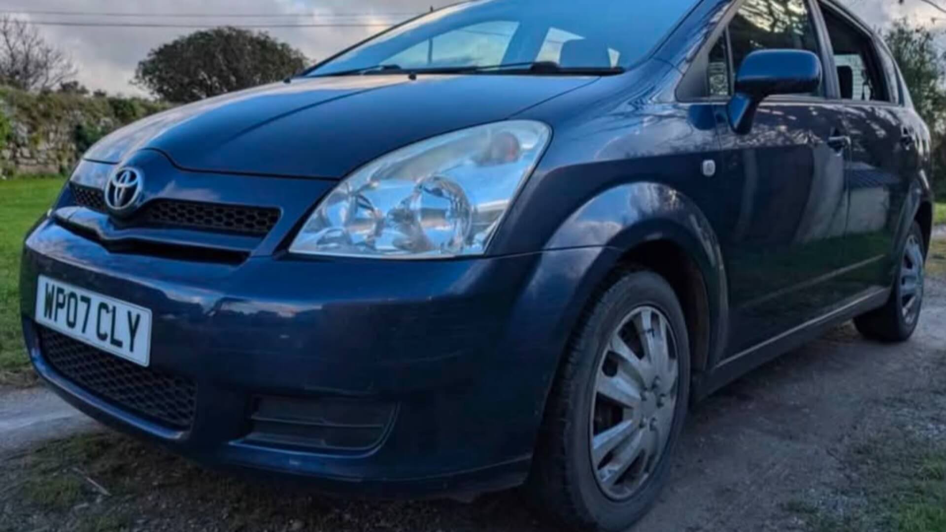 An ageing dark blue Toyota on an '07 plate parked beside a Cornish hedge, the car two youth workers are driving to Benidorm