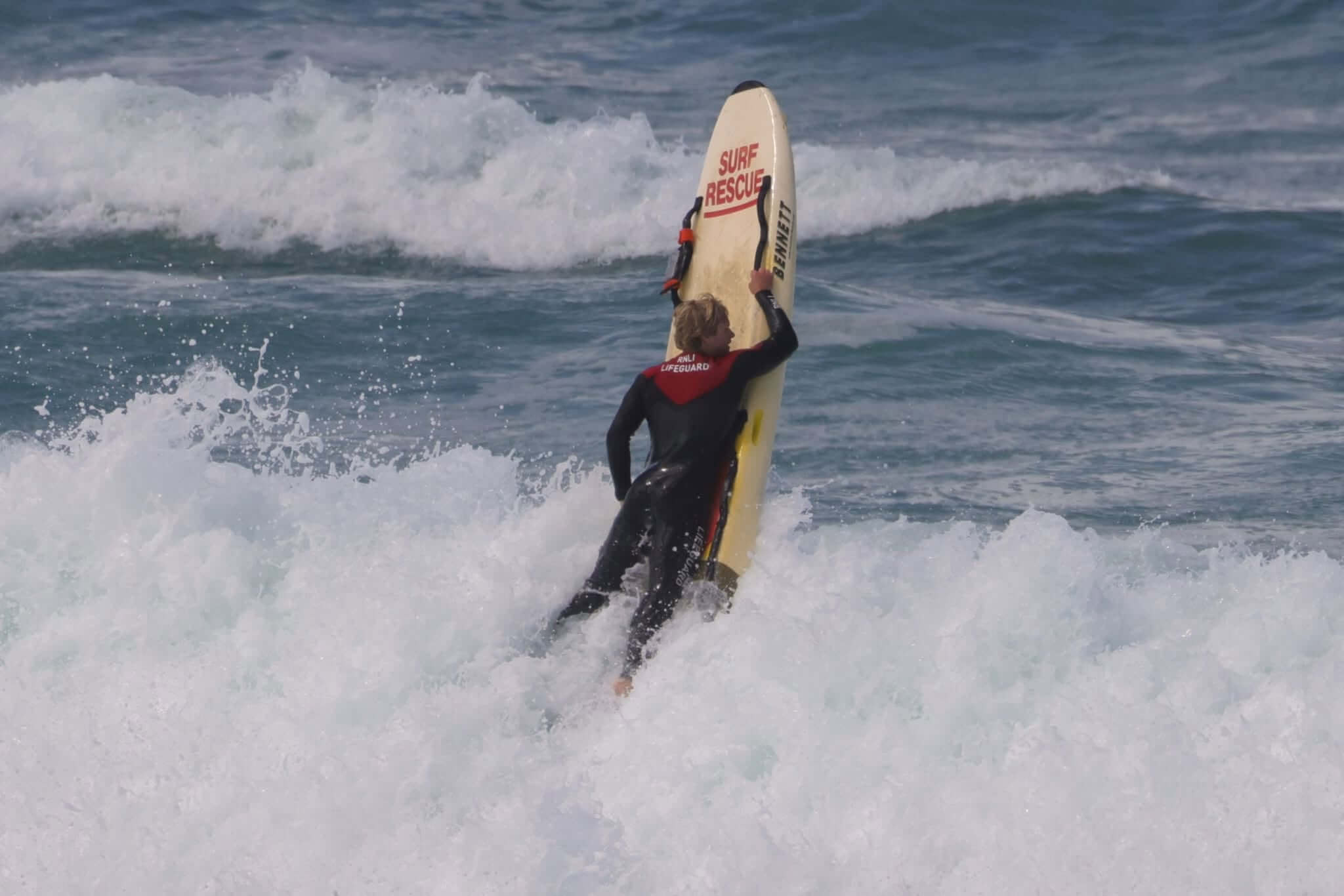 RNLI lifeguard carrying a surf rescue board through breaking waves
