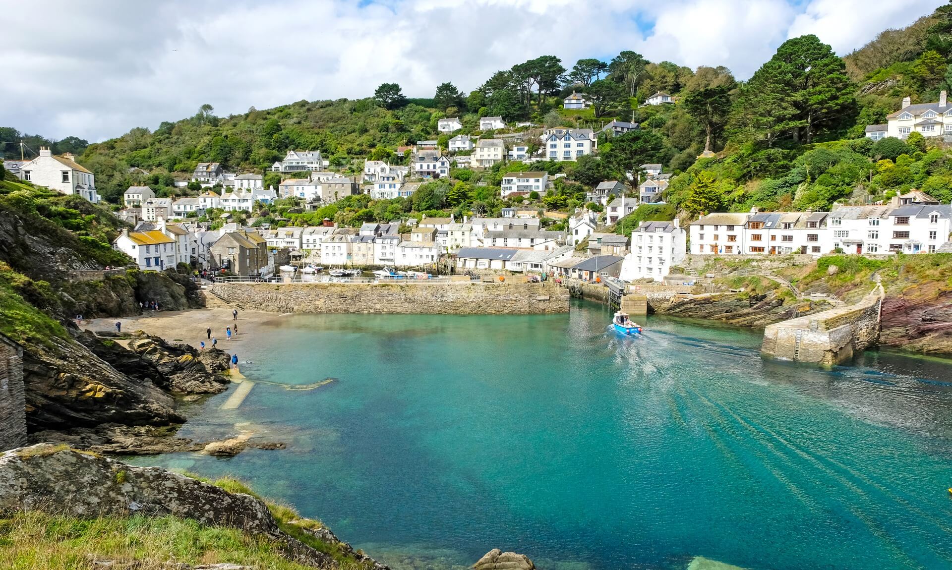 Polperro harbour with a blue fishing boat coming in past whitewashed cottages on the hillside
