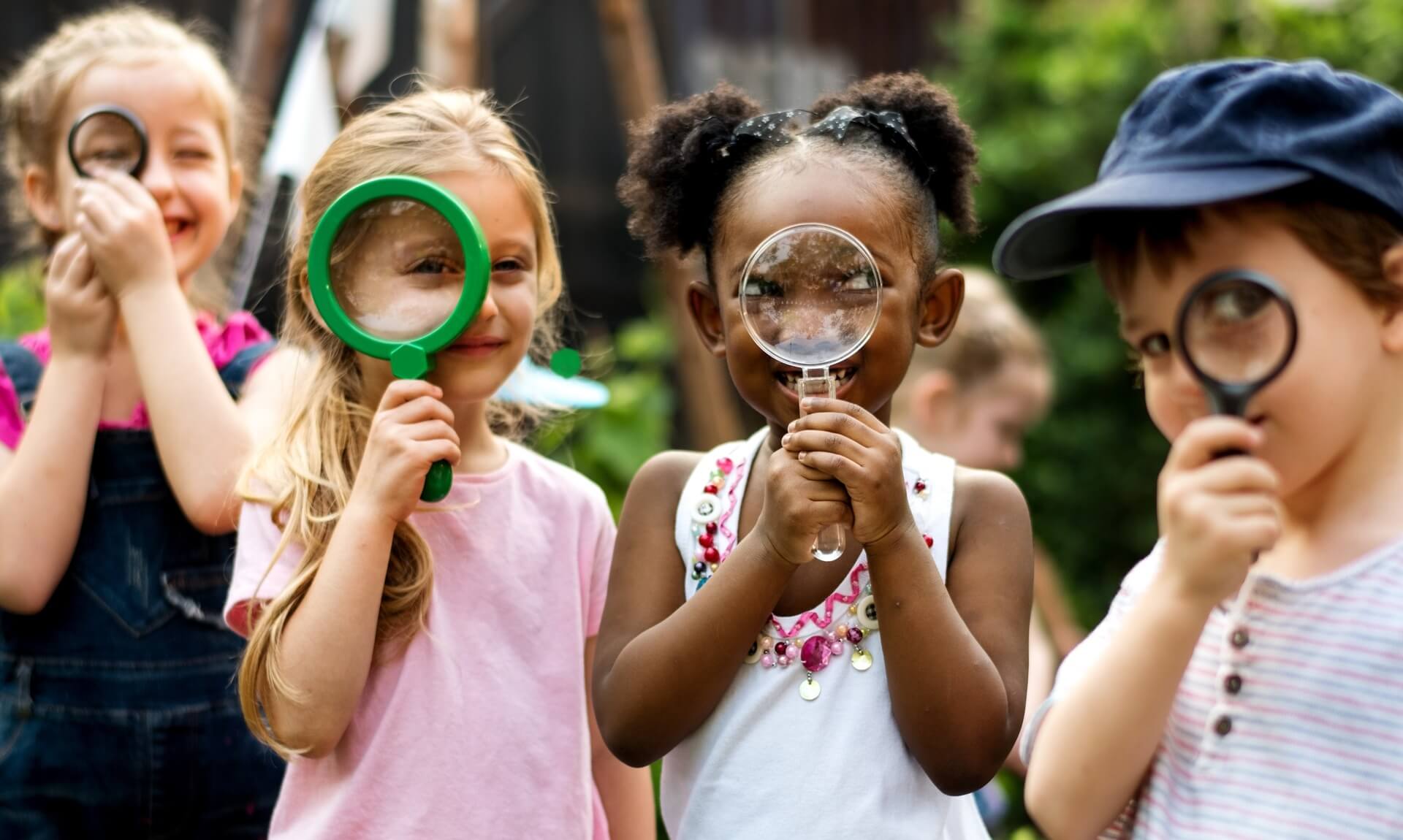 Four young children looking through magnifying glasses in a garden