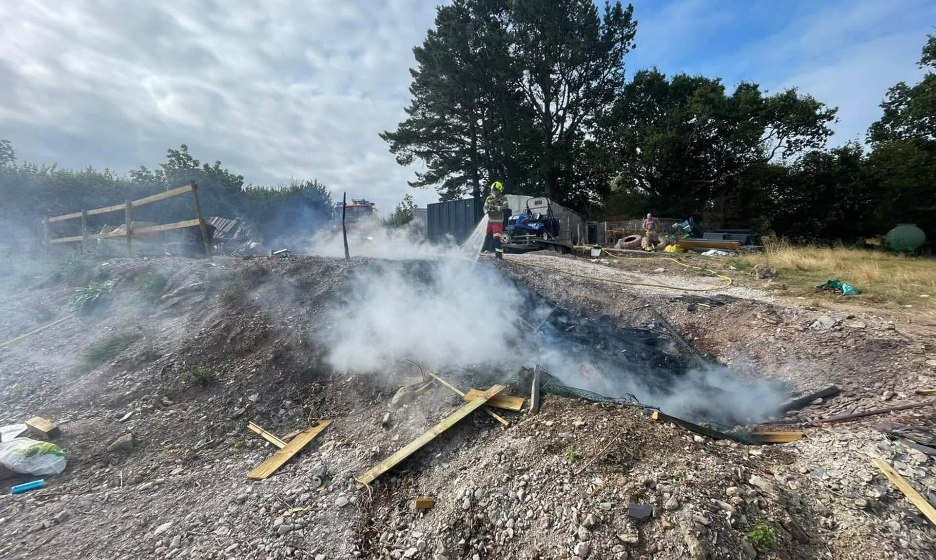 Firefighter damping down a smouldering bonfire on rough ground in Saltash