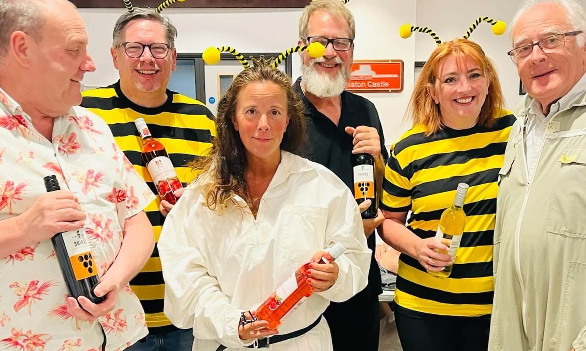 Costumed quiz-goers holding wine-bottle prizes under the Saltash sign