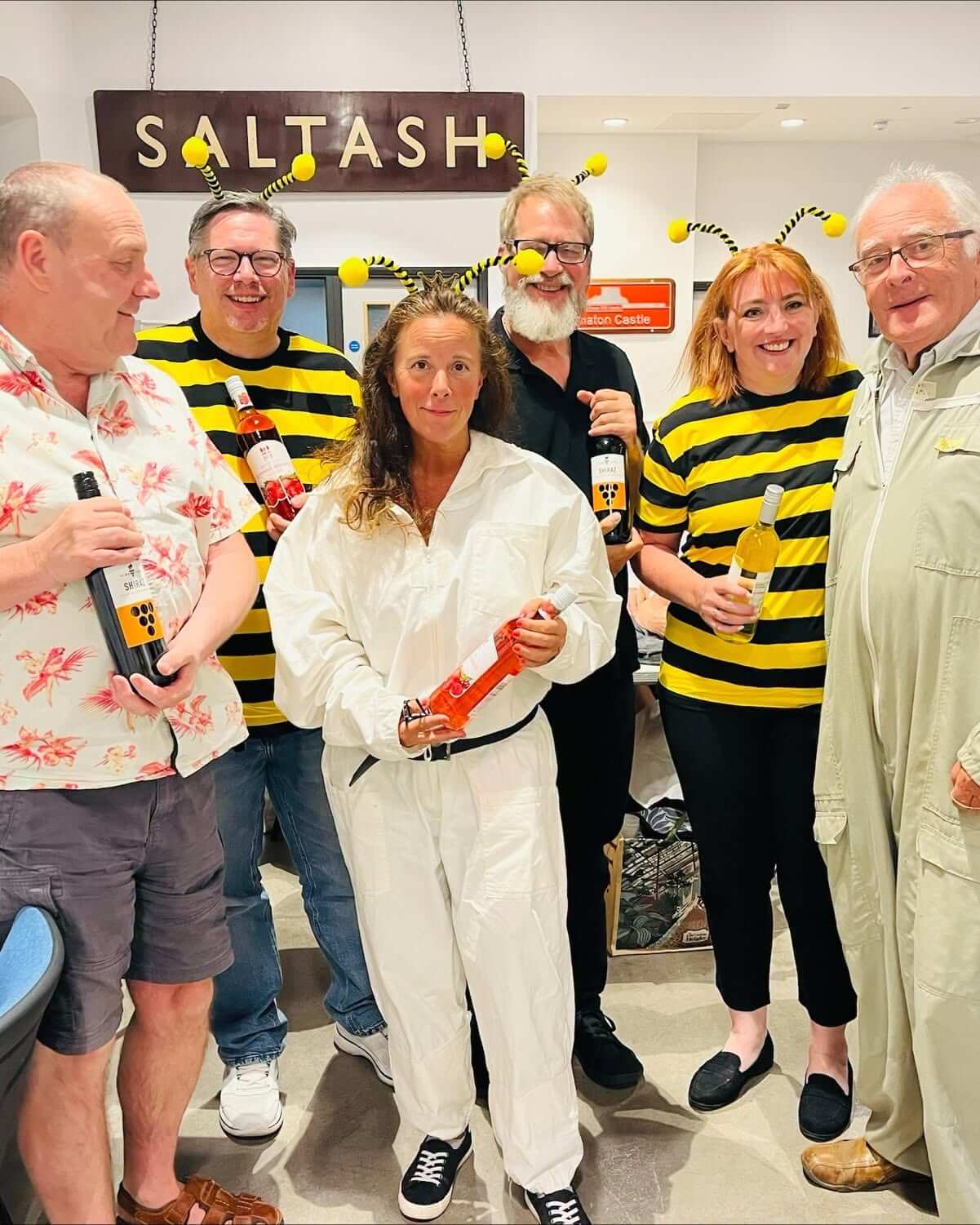 Costumed quiz-goers holding wine-bottle prizes under the Saltash sign