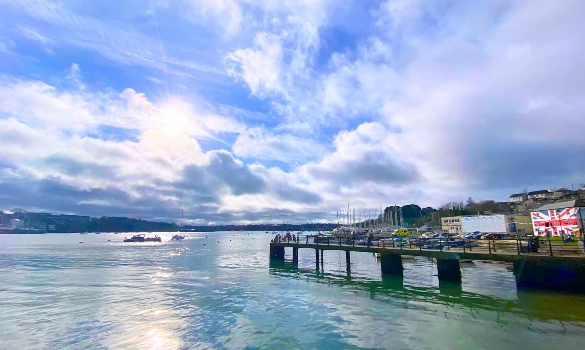 Sunlit view across Saltash Waterside with the pontoon, moored boats and the sailing club