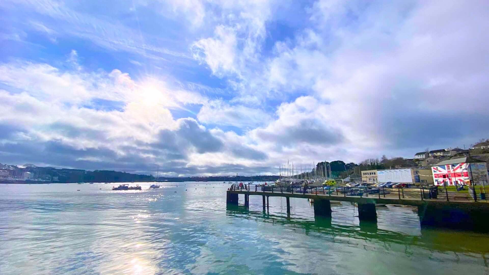 Sunlit view across Saltash Waterside with the pontoon, moored boats and the sailing club