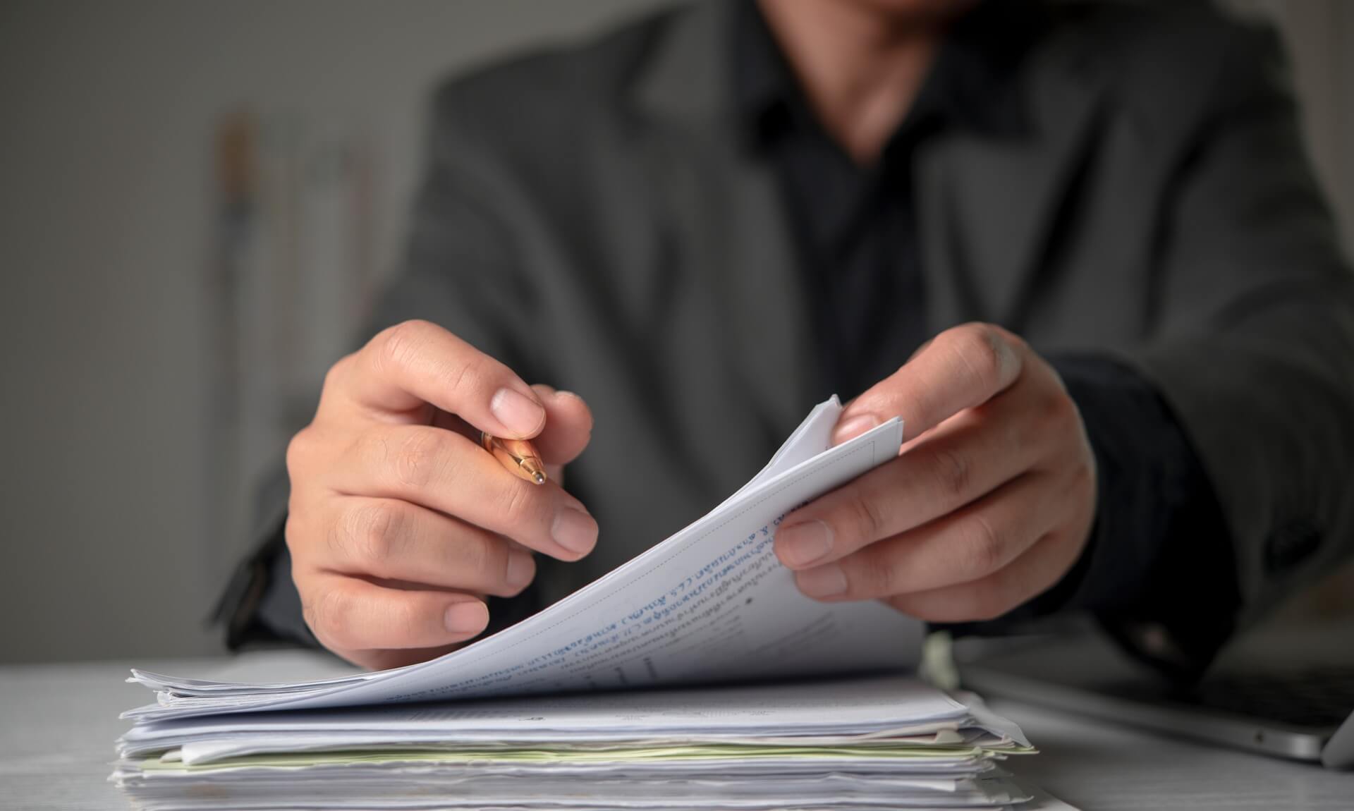 Business owner in a suit reviewing a thick stack of documents with a pen